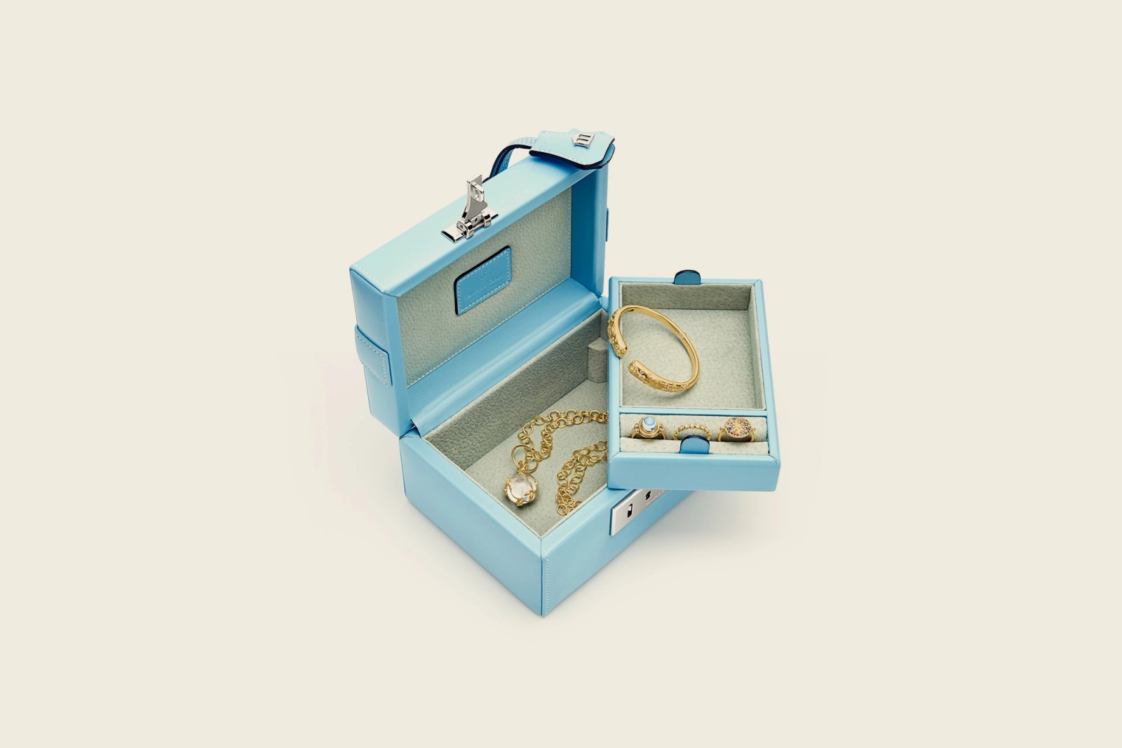 An open light blue jewelry box containing a gold necklace, bangle, and rings.