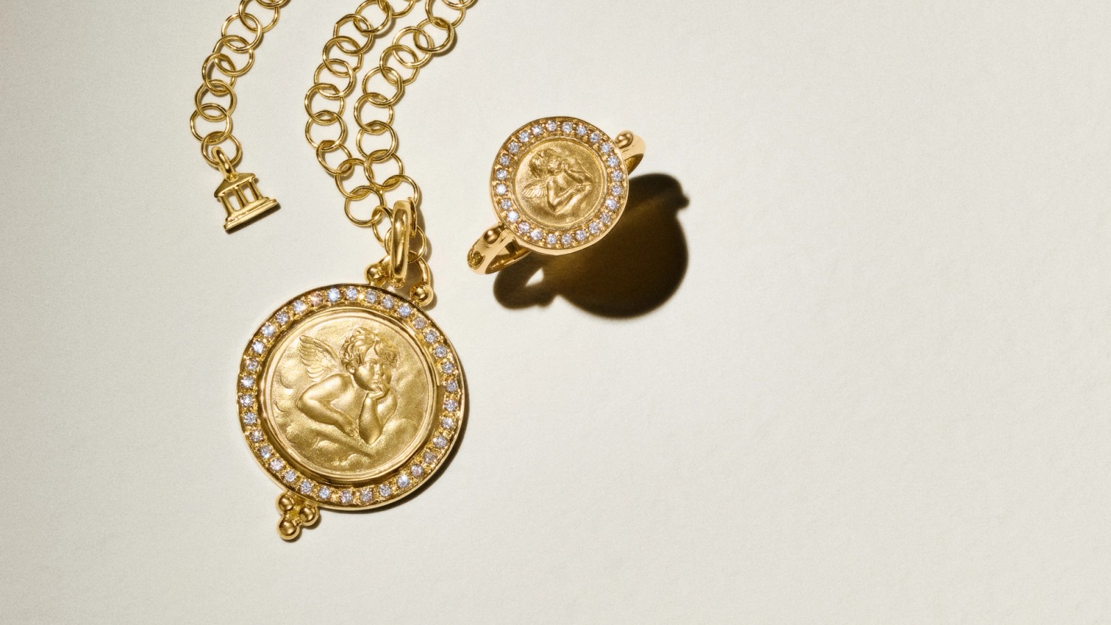 A gold cherub pendant with a diamond halo on a chain, next to a matching cherub ring.