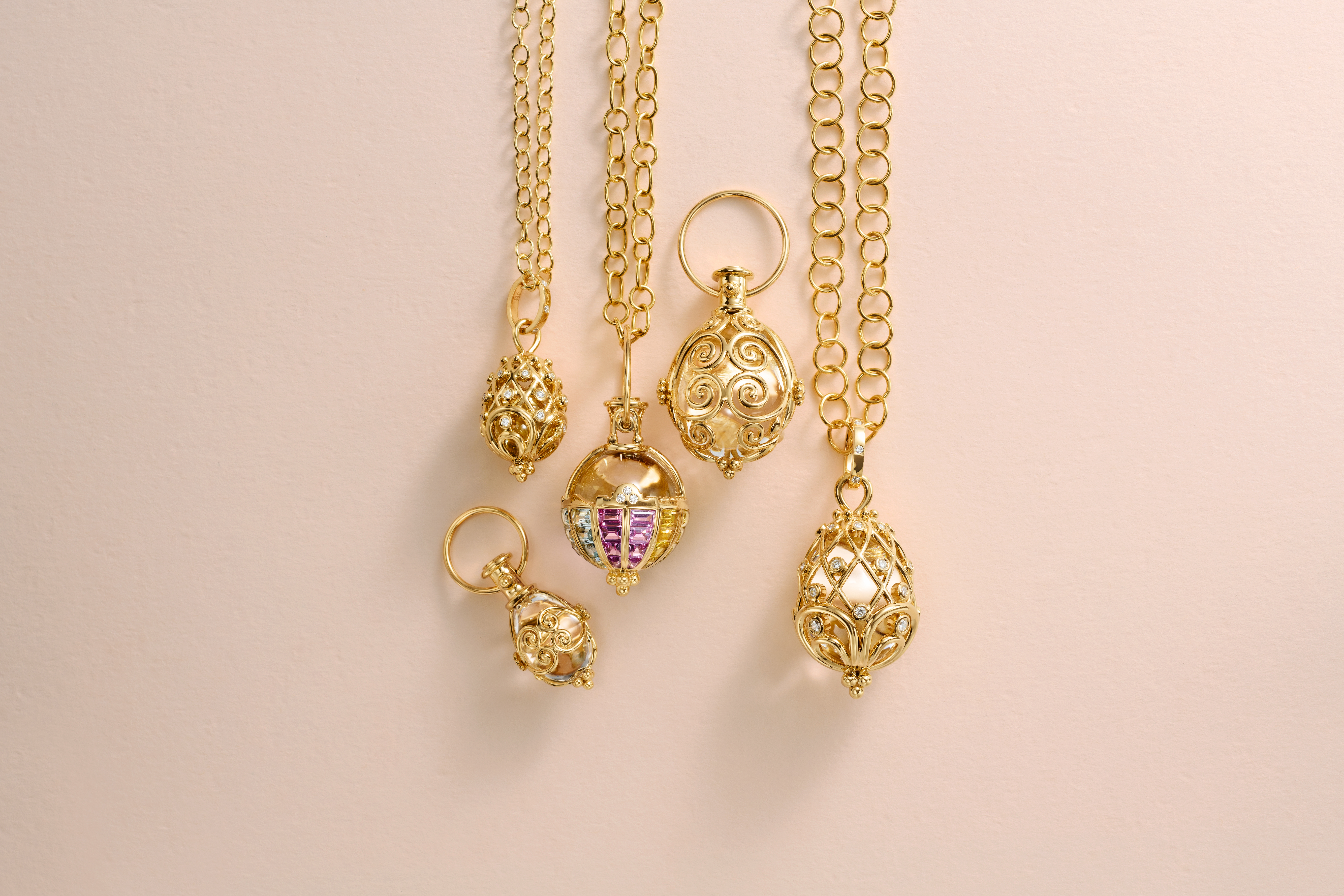Five ornate gold pendants, some with colorful gems, hanging on a light pink background.
