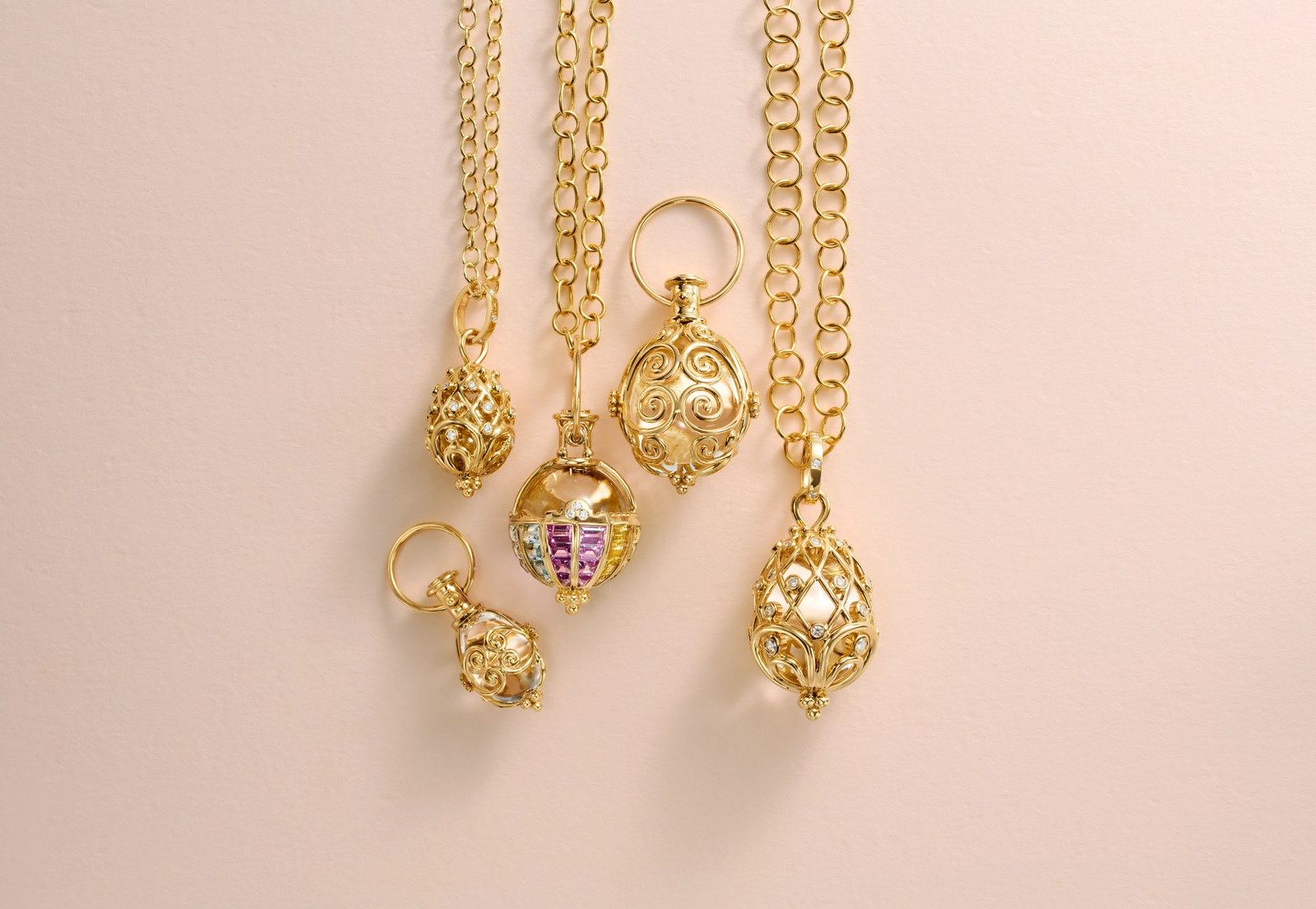 Five ornate gold pendants, some with colorful gems, hanging on a light pink background.