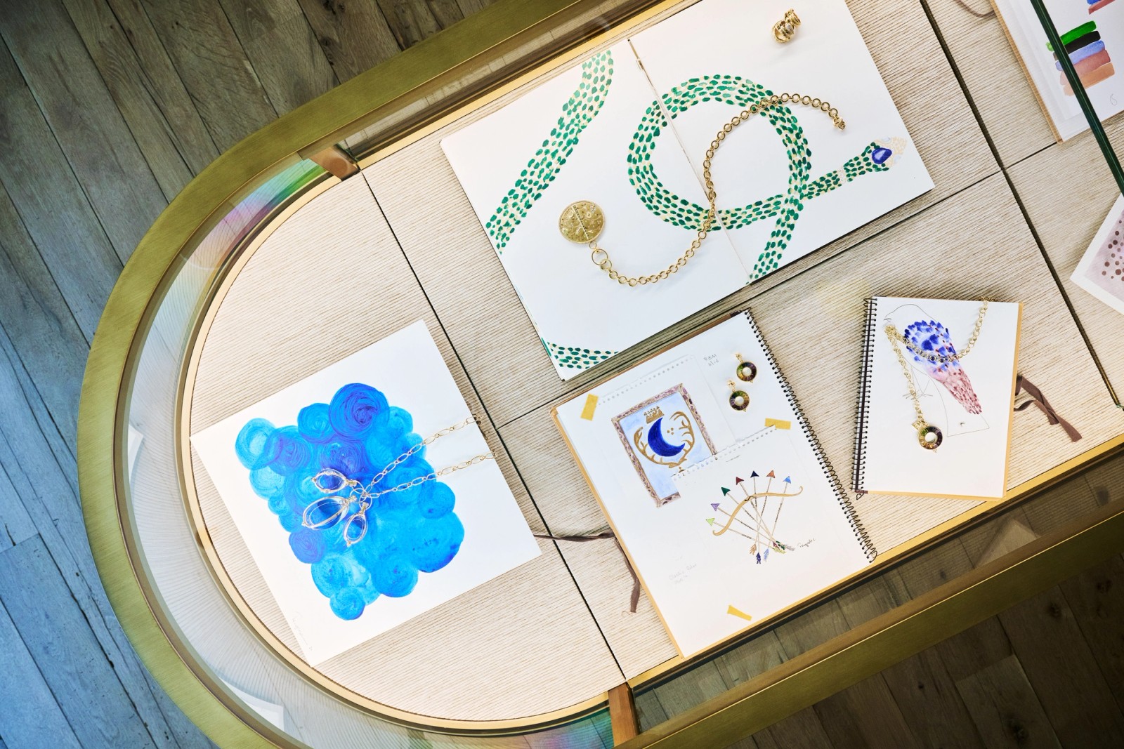Jewelry design sketches and necklaces displayed in a gold-framed case.