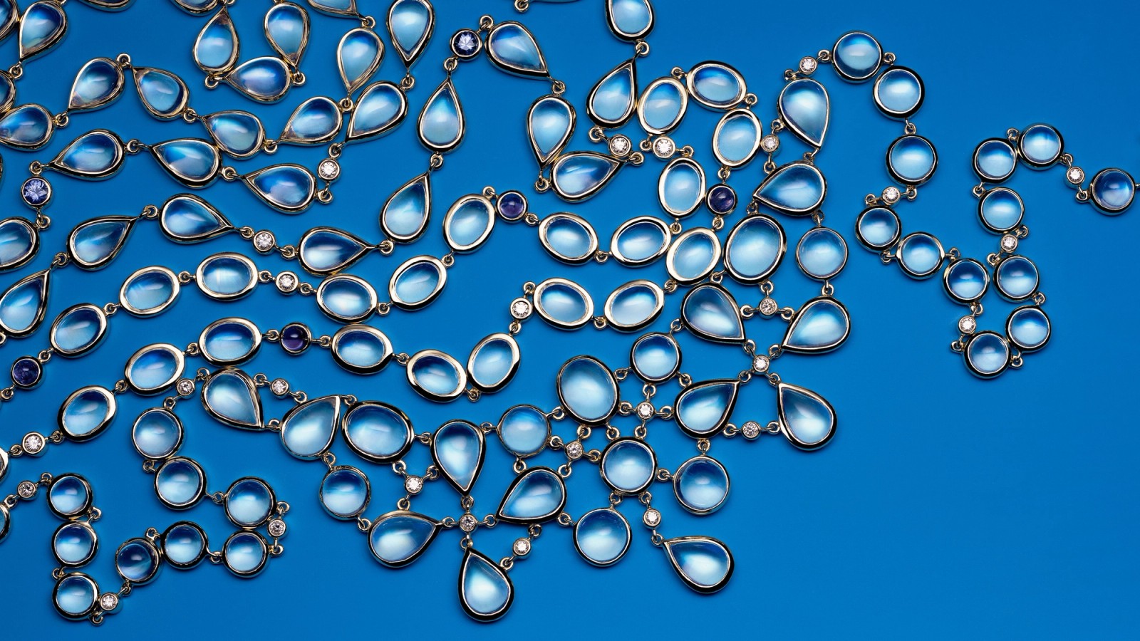 Multiple strands of light blue translucent gemstones with small accent stones on a blue background.