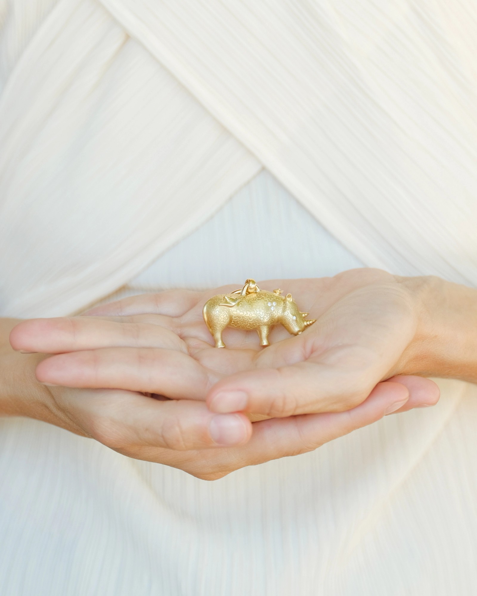 Hands holding a sparkling golden rhino charm.