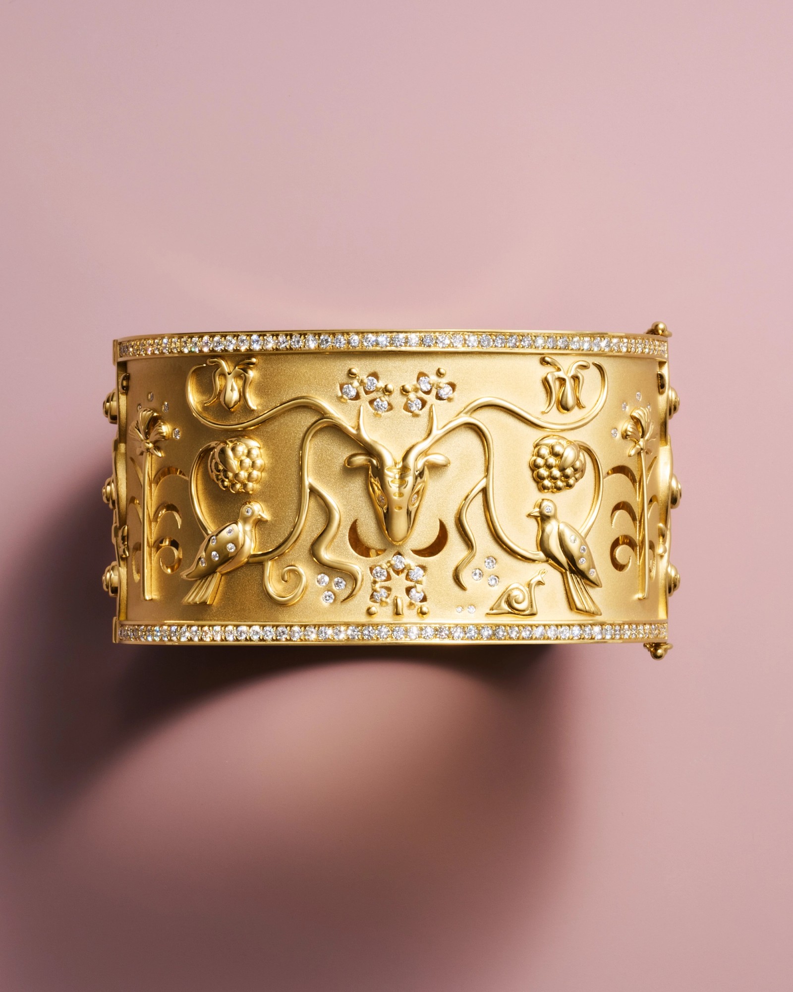 Ornate gold cuff bracelet featuring an embossed deer head, birds, vines, and diamond-studded edges.