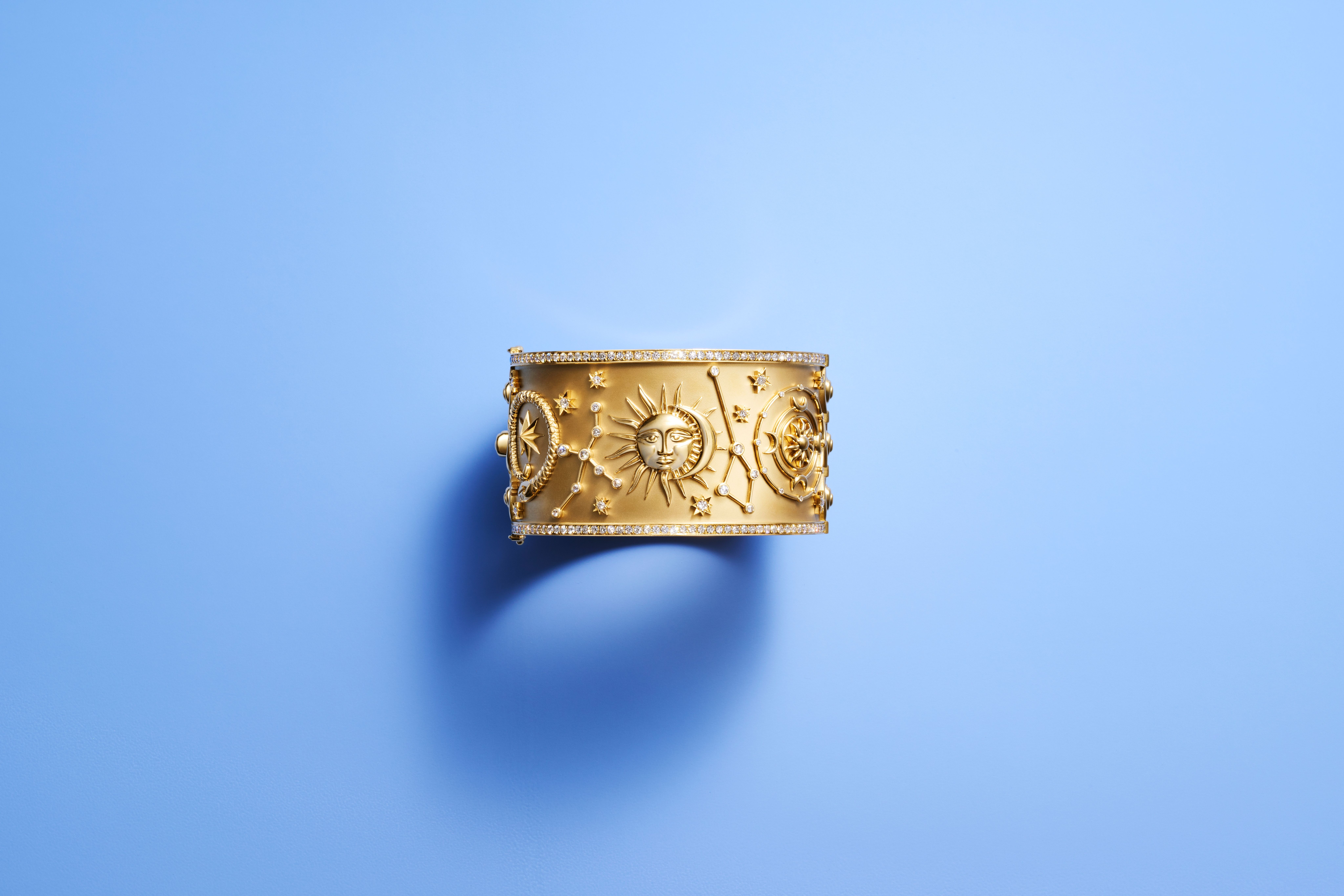 Gold cuff bracelet featuring embossed sun, moon, stars, constellations, and compass rose designs, accented with diamonds.