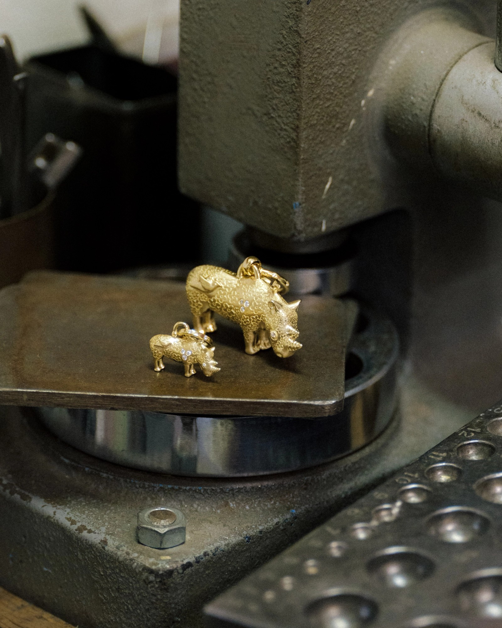 Two gold rhinoceros charms, one large and one small, with diamond details, sit on a metal workbench.