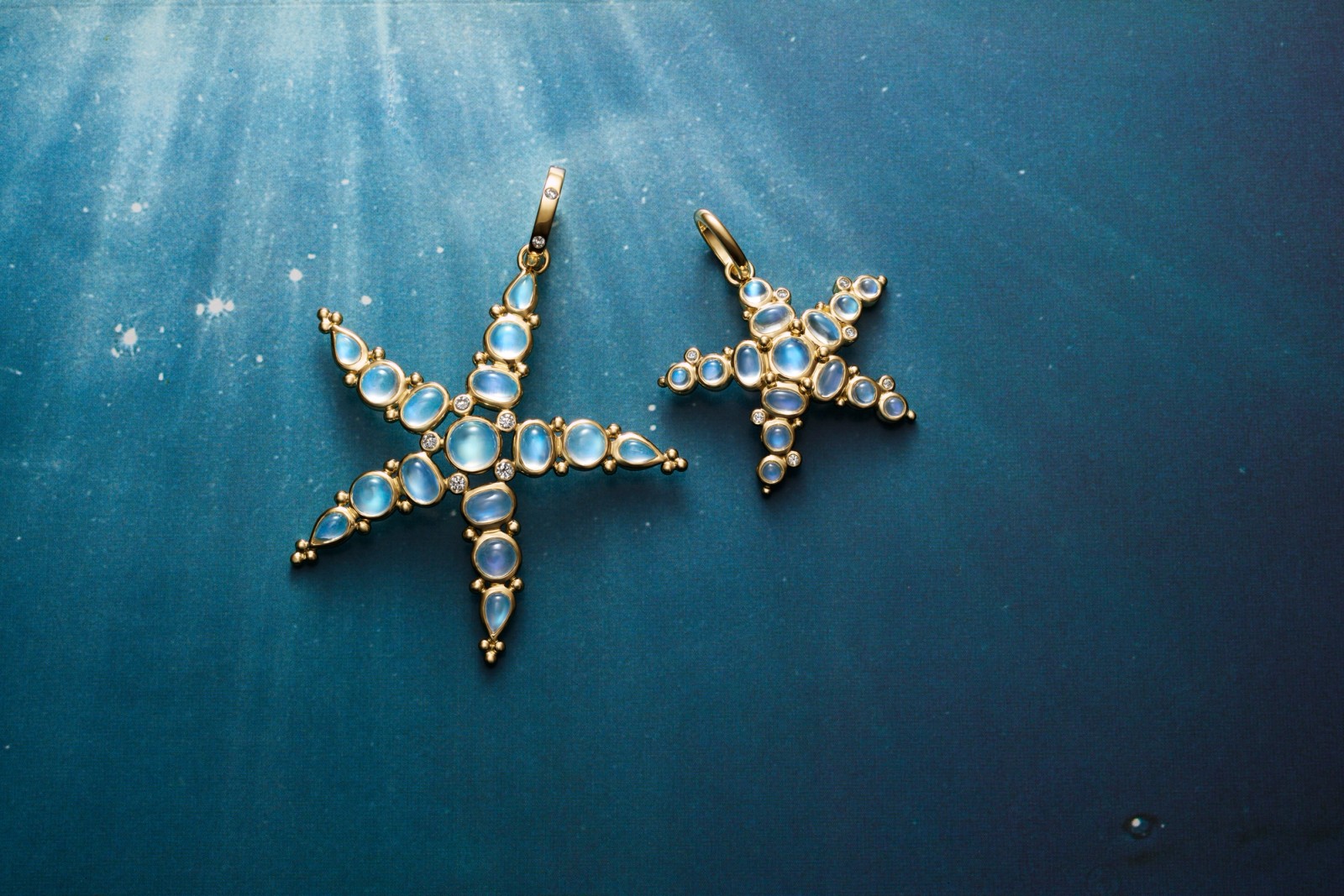 Two gold starfish-shaped jewelry pieces with blue moonstones and diamonds on a shimmering blue background.