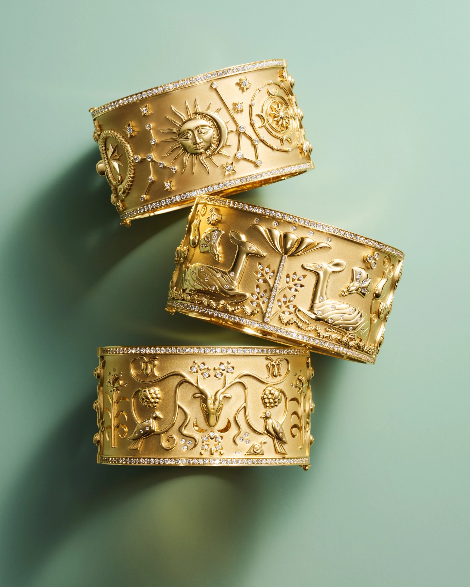Three ornate gold cuff bracelets with diamond trim, featuring celestial, nature, and animal motifs.