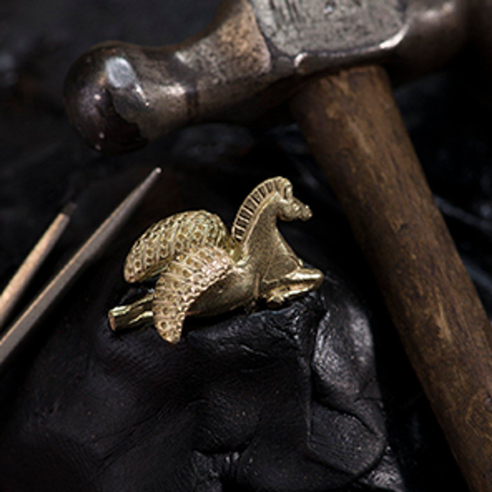A golden Pegasus figurine on a dark surface with crafting tools.