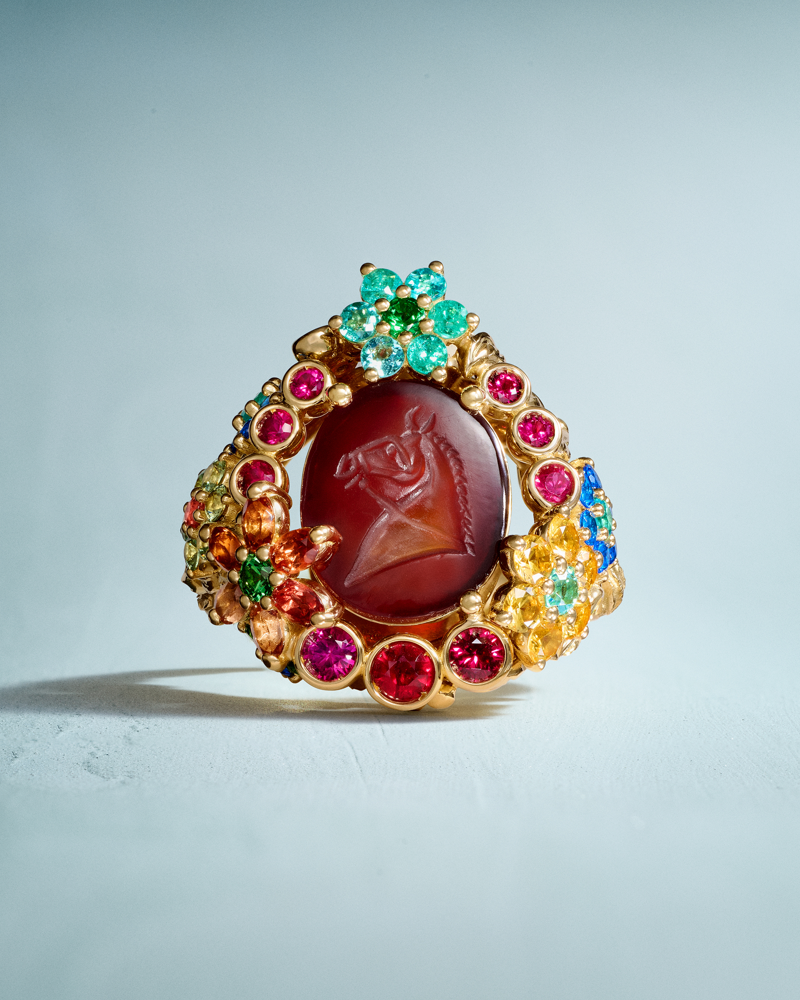 Ornate gold ring featuring an oval reddish-brown cameo of a horse's head, framed by multicolored gemstones.