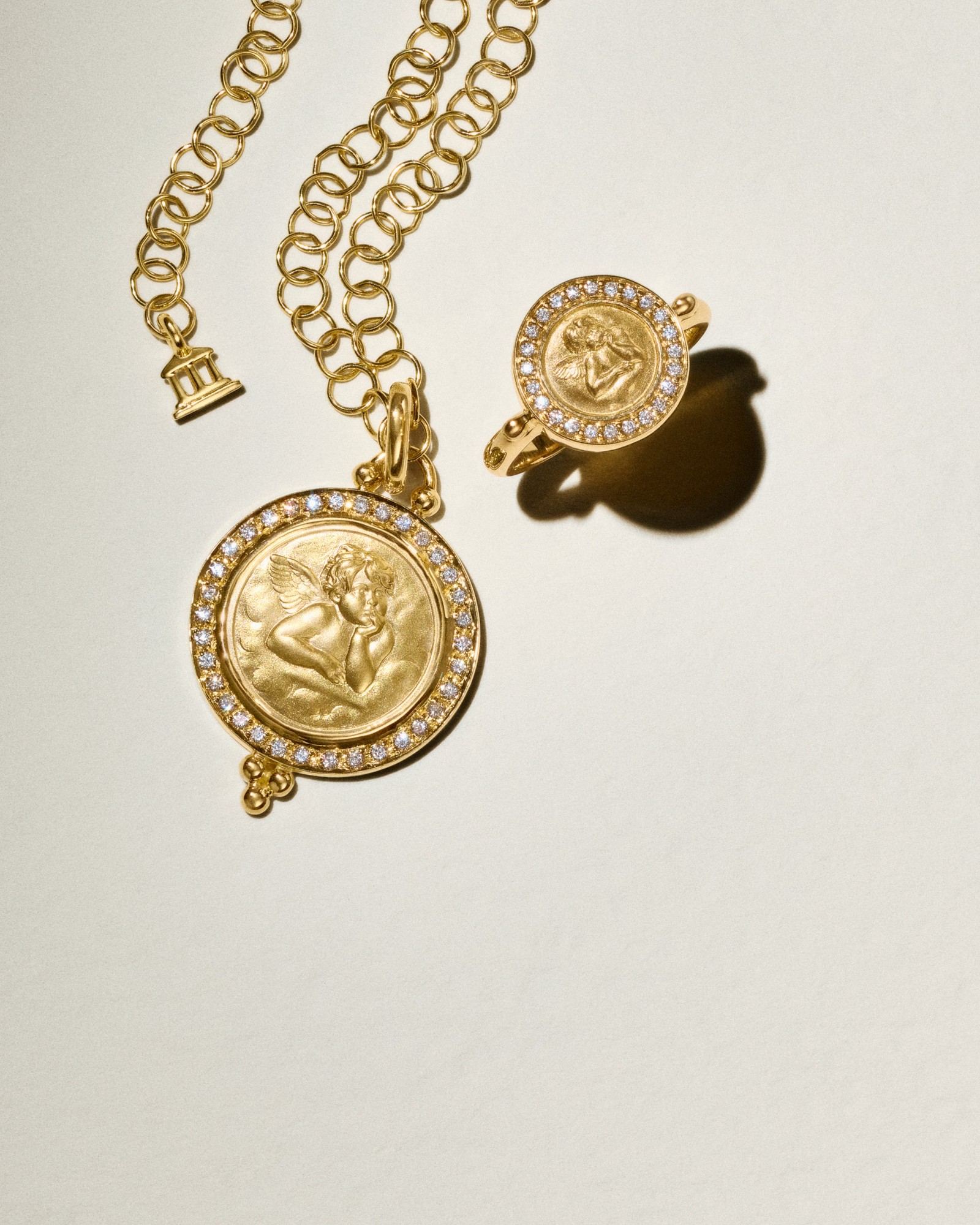 Gold necklace and ring featuring a cherub design encircled by diamonds.