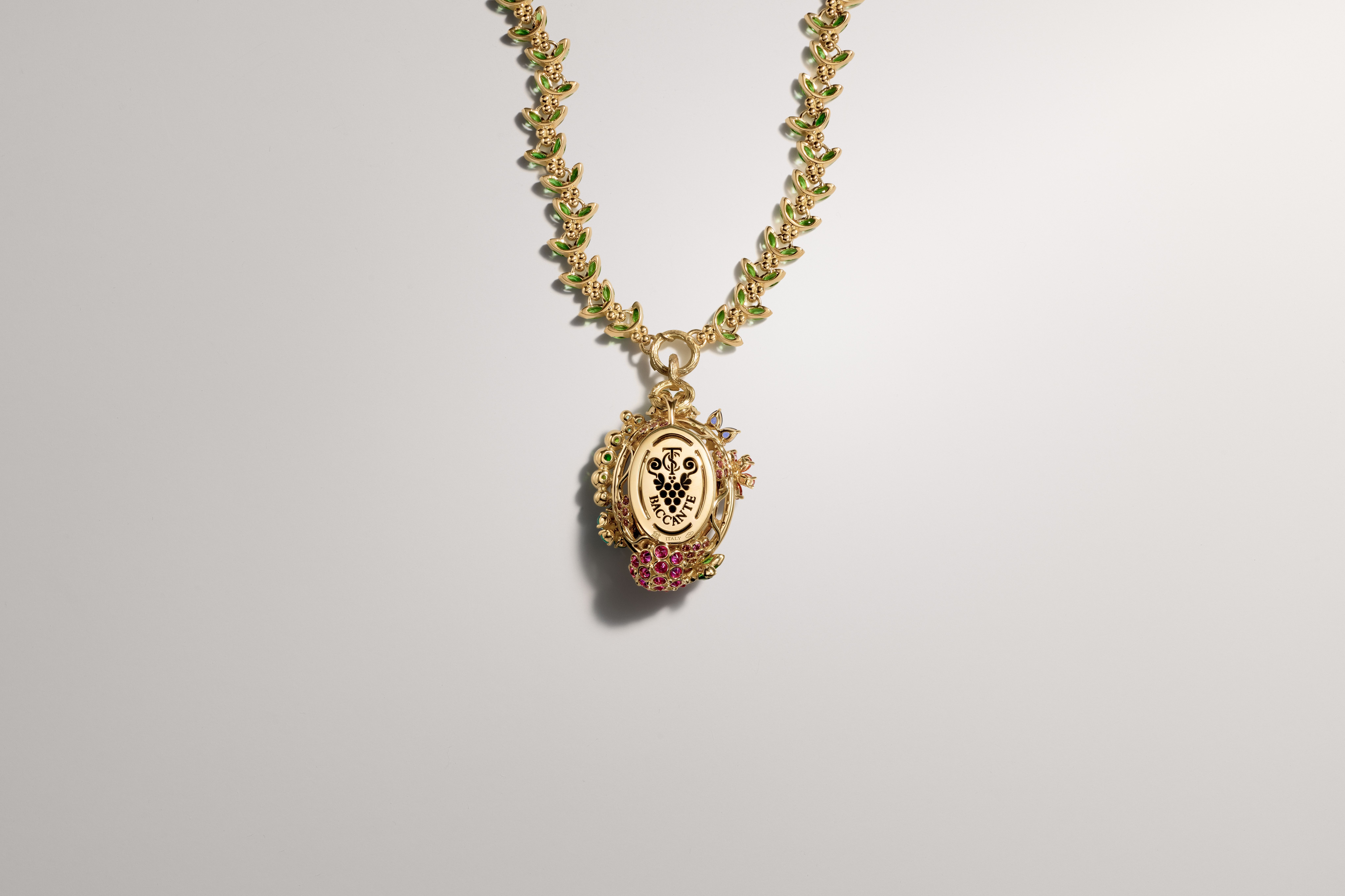 Gold necklace with green enamel leaves and an ornate pendant featuring a white oval with a black design, adorned with red gemstones.