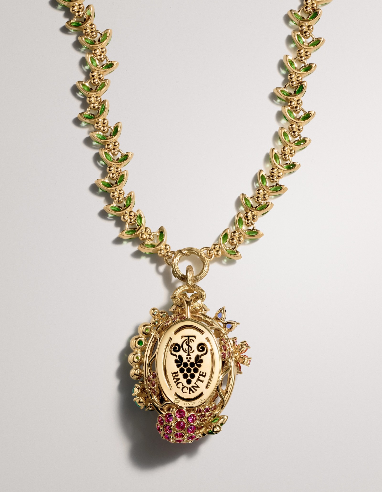 Gold necklace with green enamel leaves and an ornate pendant featuring a white oval with a black design, adorned with red gemstones.