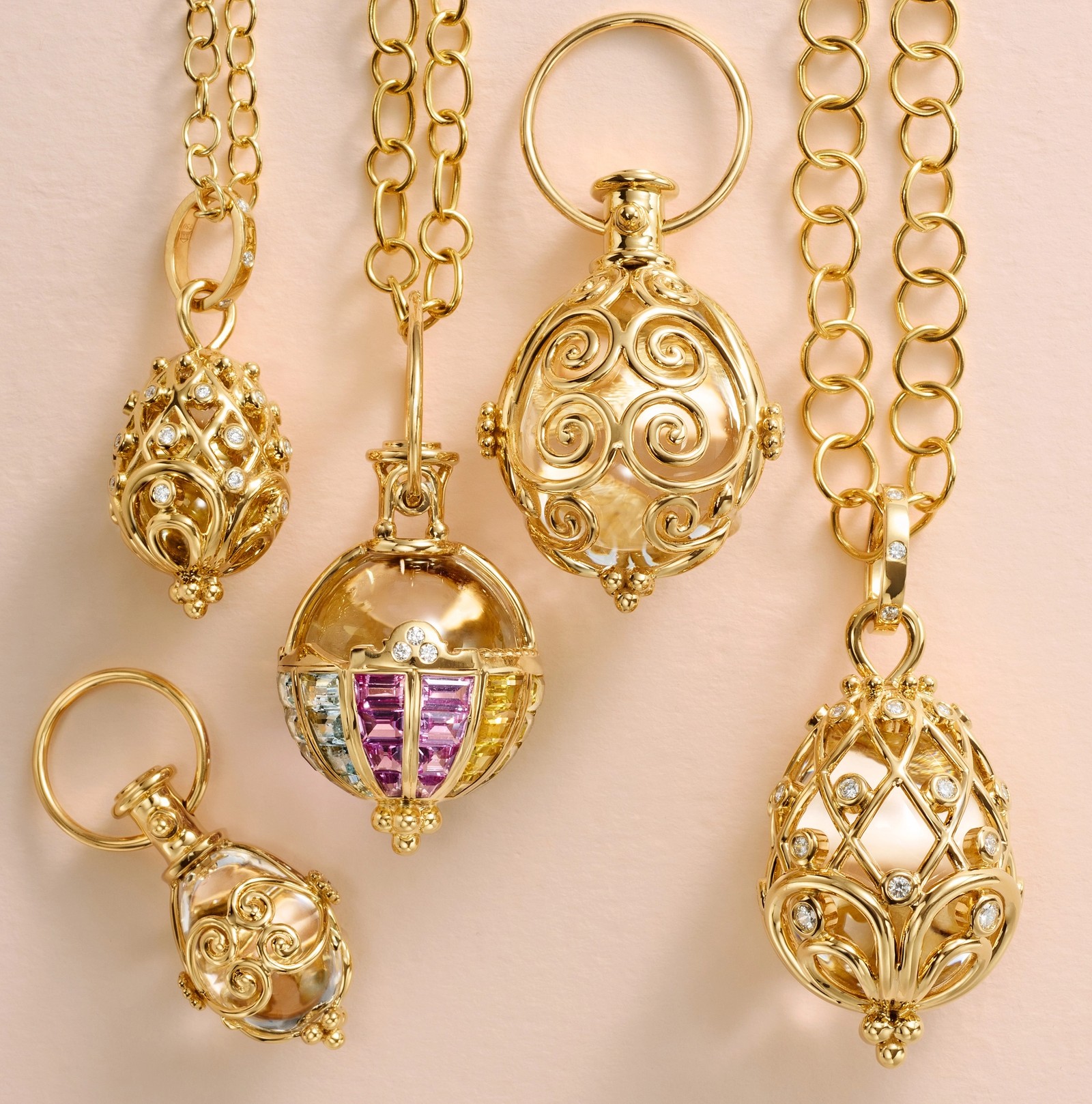 A collection of five ornate gold pendants featuring filigree, diamonds, pearls, and colorful gemstones, hanging from gold chains against a pink background.