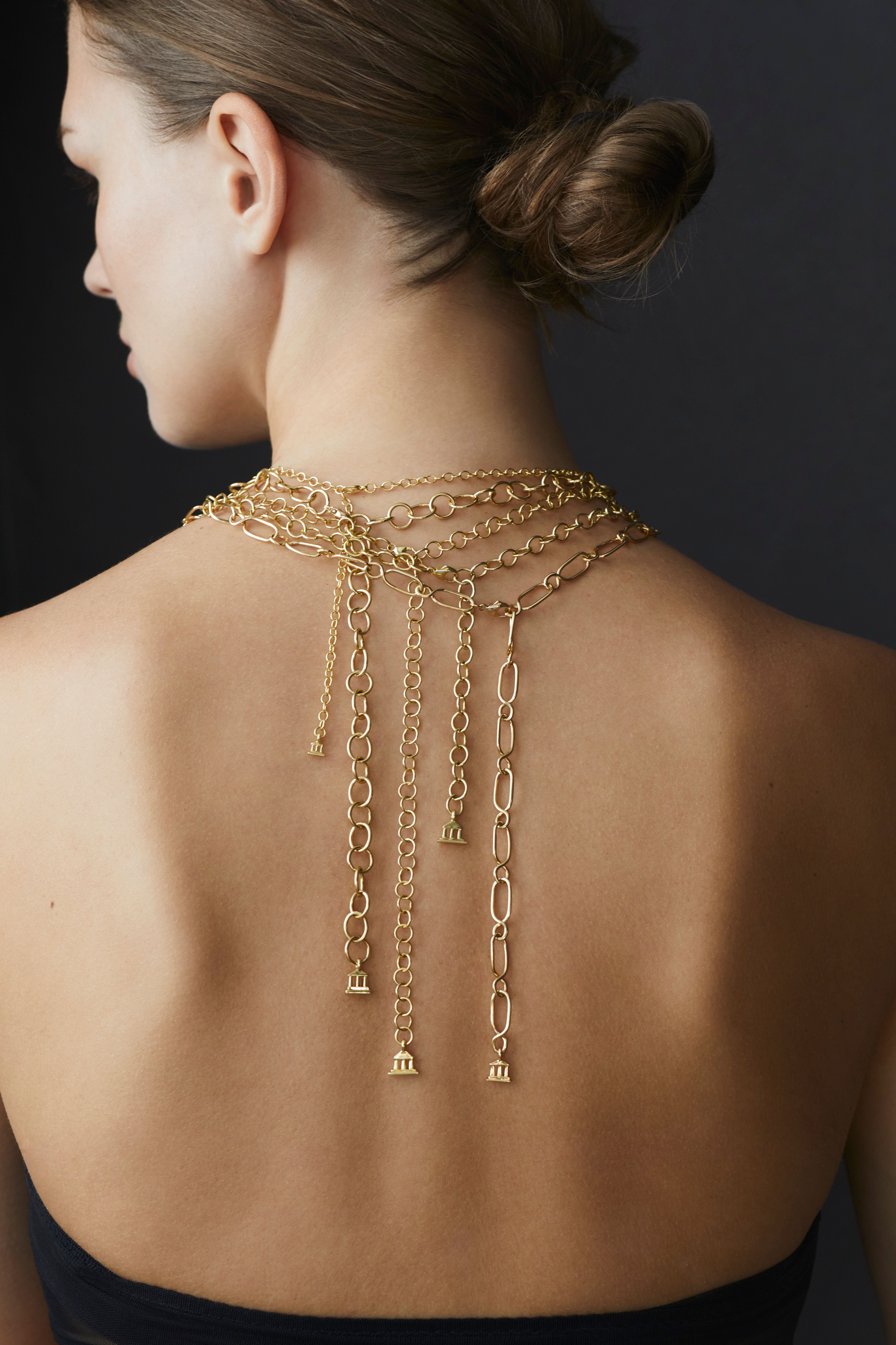 A woman's back adorned with multiple gold chains draped downwards, her hair in a bun.