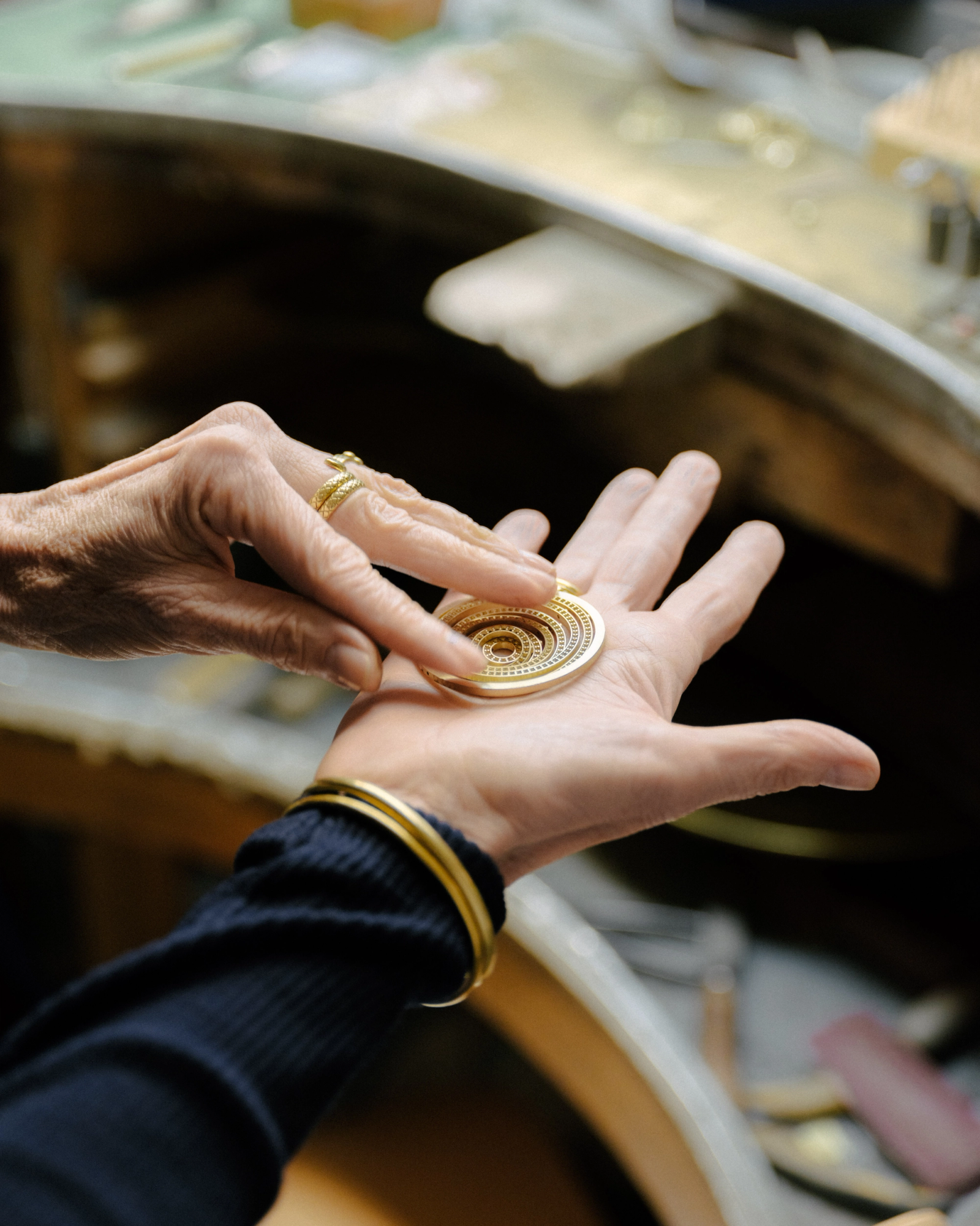 Close-up of hands examining a circular gold piece with a concentric spiral pattern.