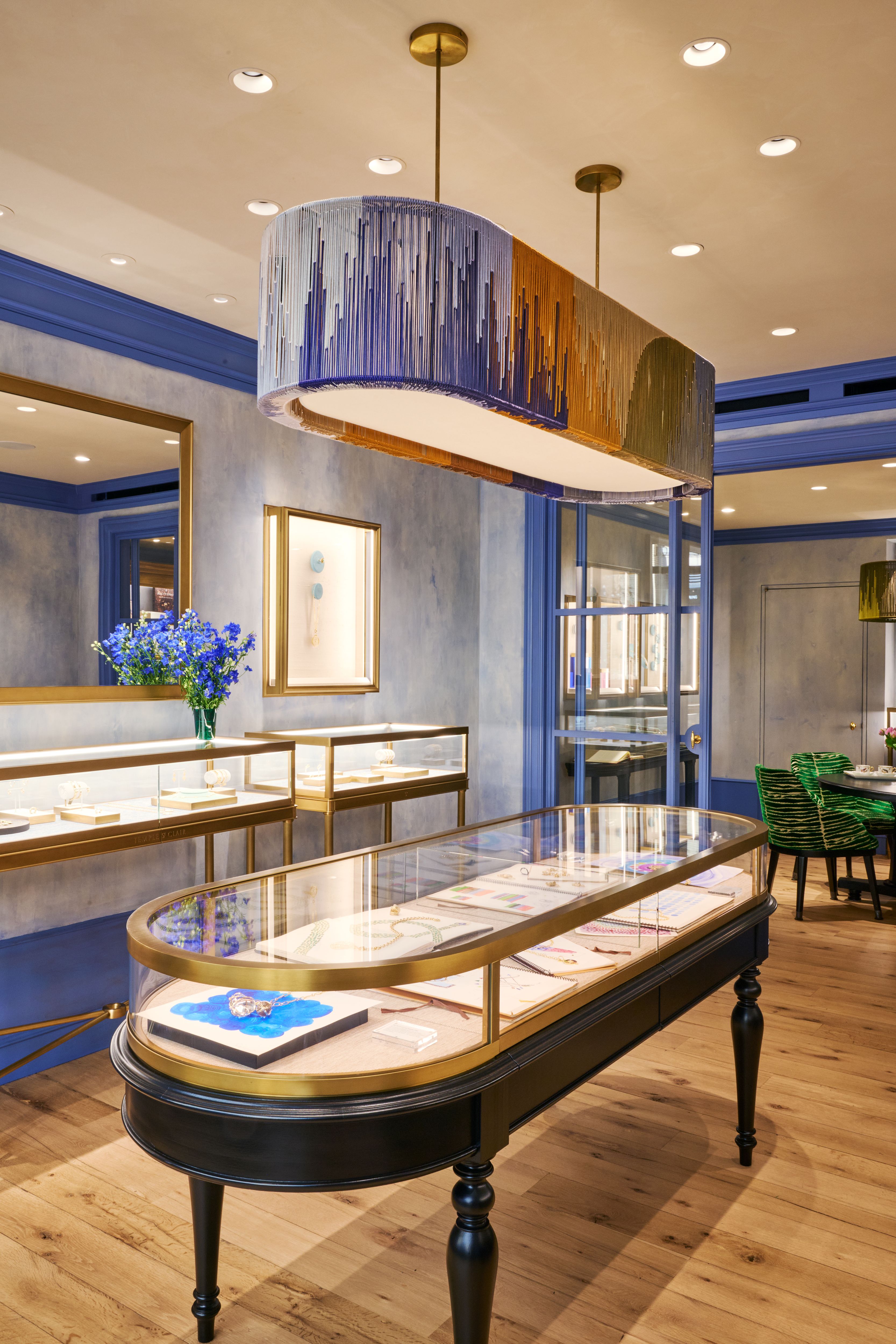 Interior of a jewelry store with an oval, fringed chandelier in blue, gold, and green, multiple display cases, and blue walls.
