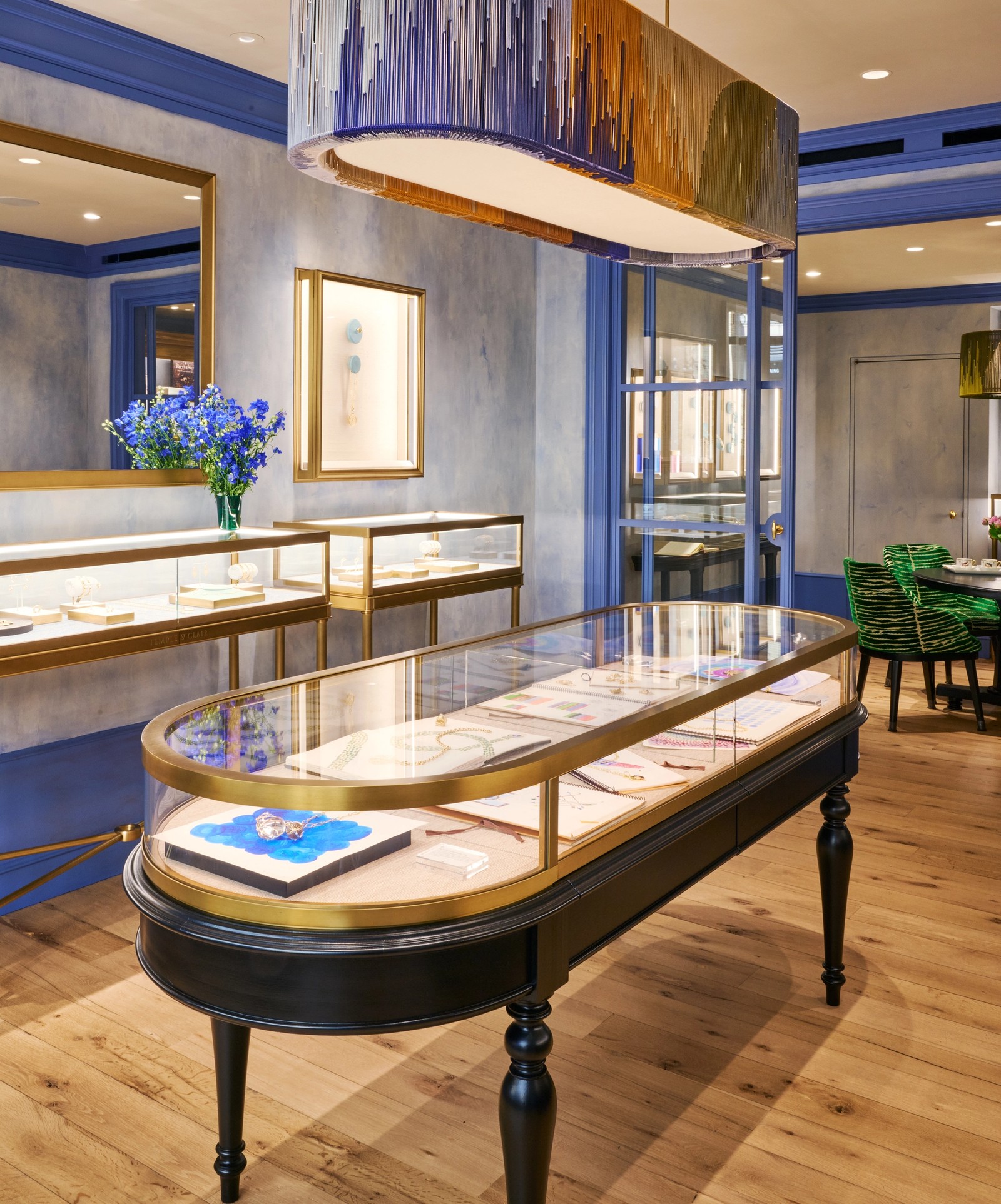 Interior of a jewelry store with an oval, fringed chandelier in blue, gold, and green, multiple display cases, and blue walls.