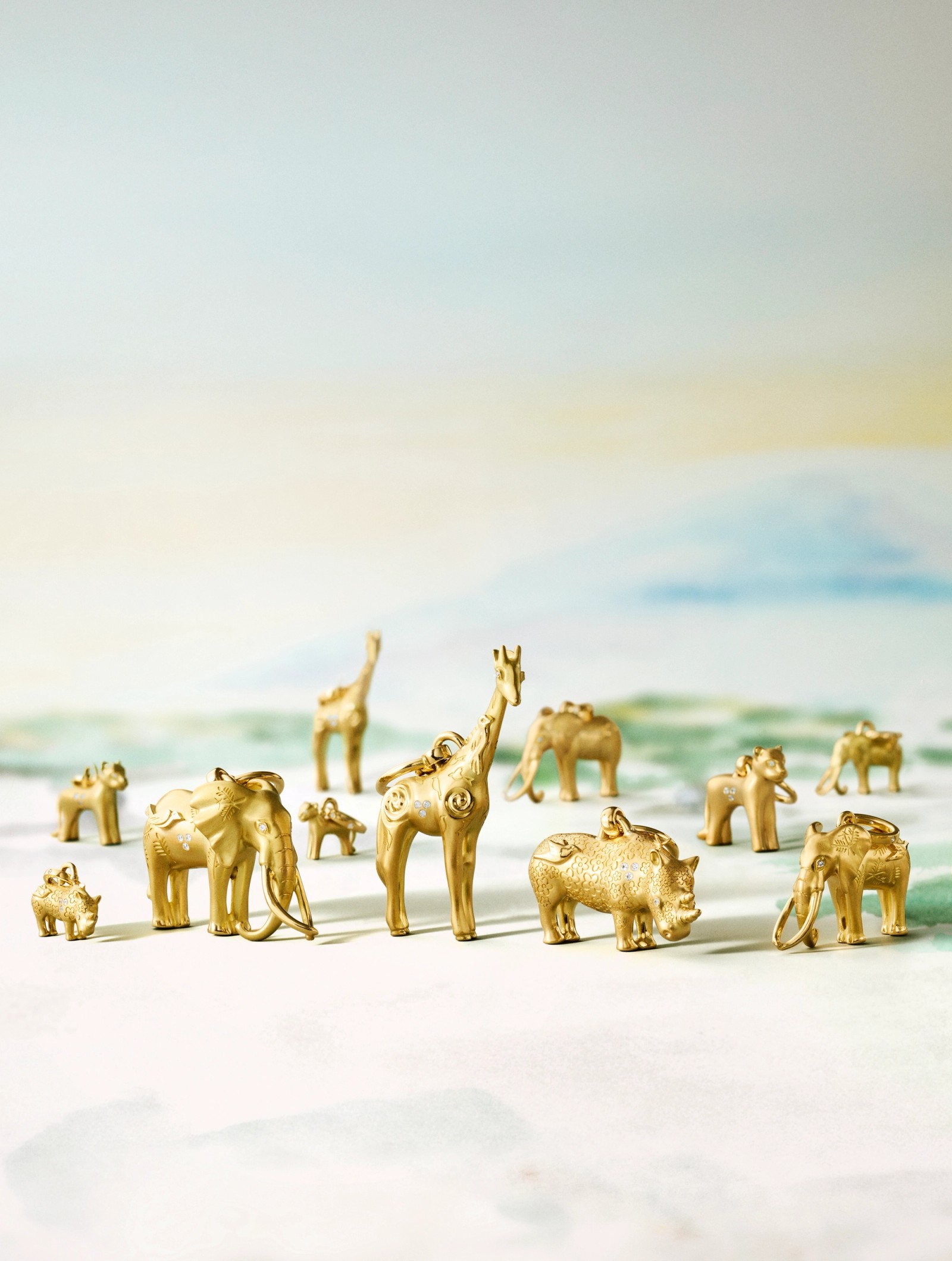 Golden elephant, giraffe, and rhino figurines with white accents on a light, blurred background.