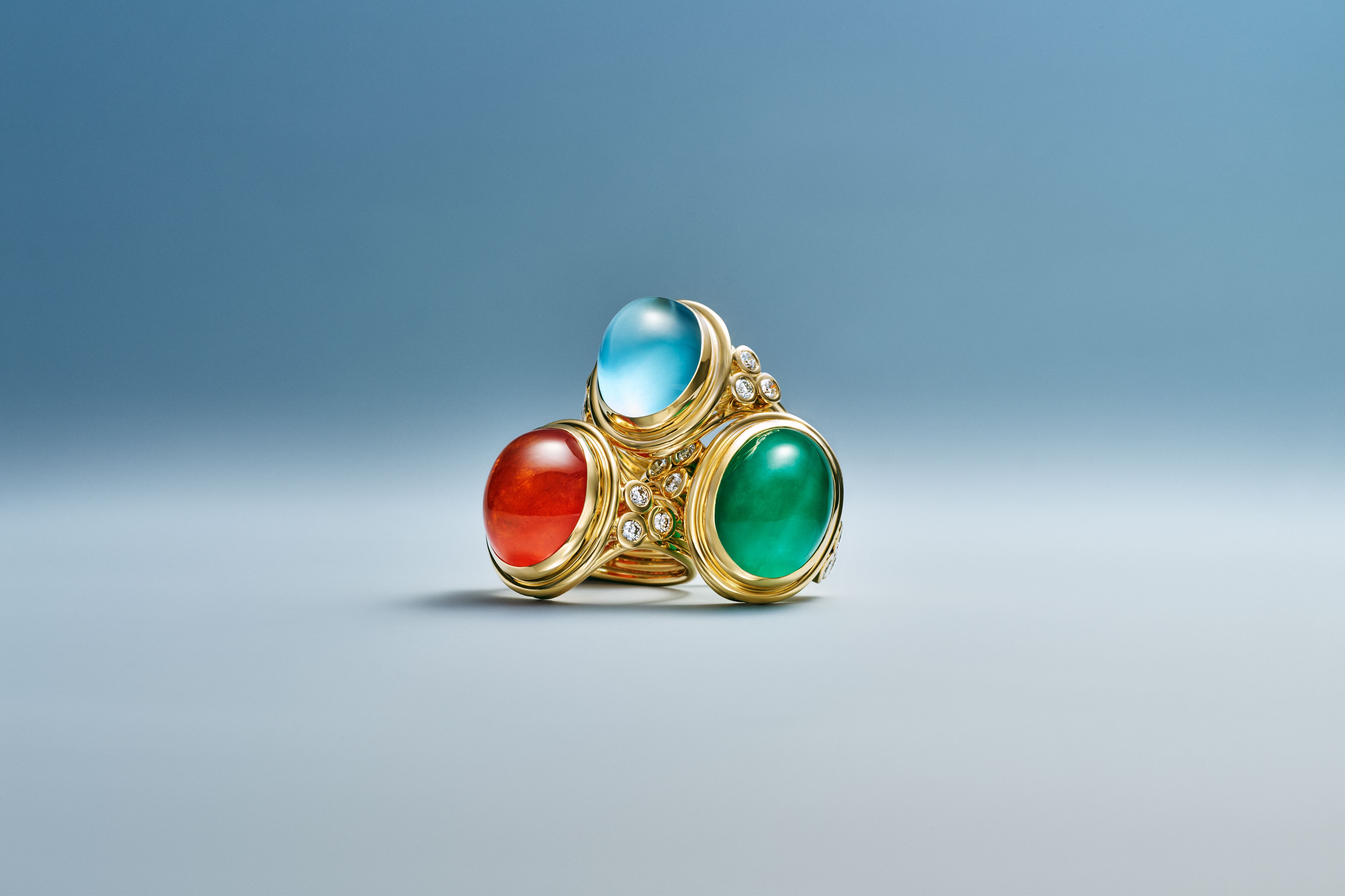 A gold ring with large blue, red, and green oval gemstones and diamond accents.