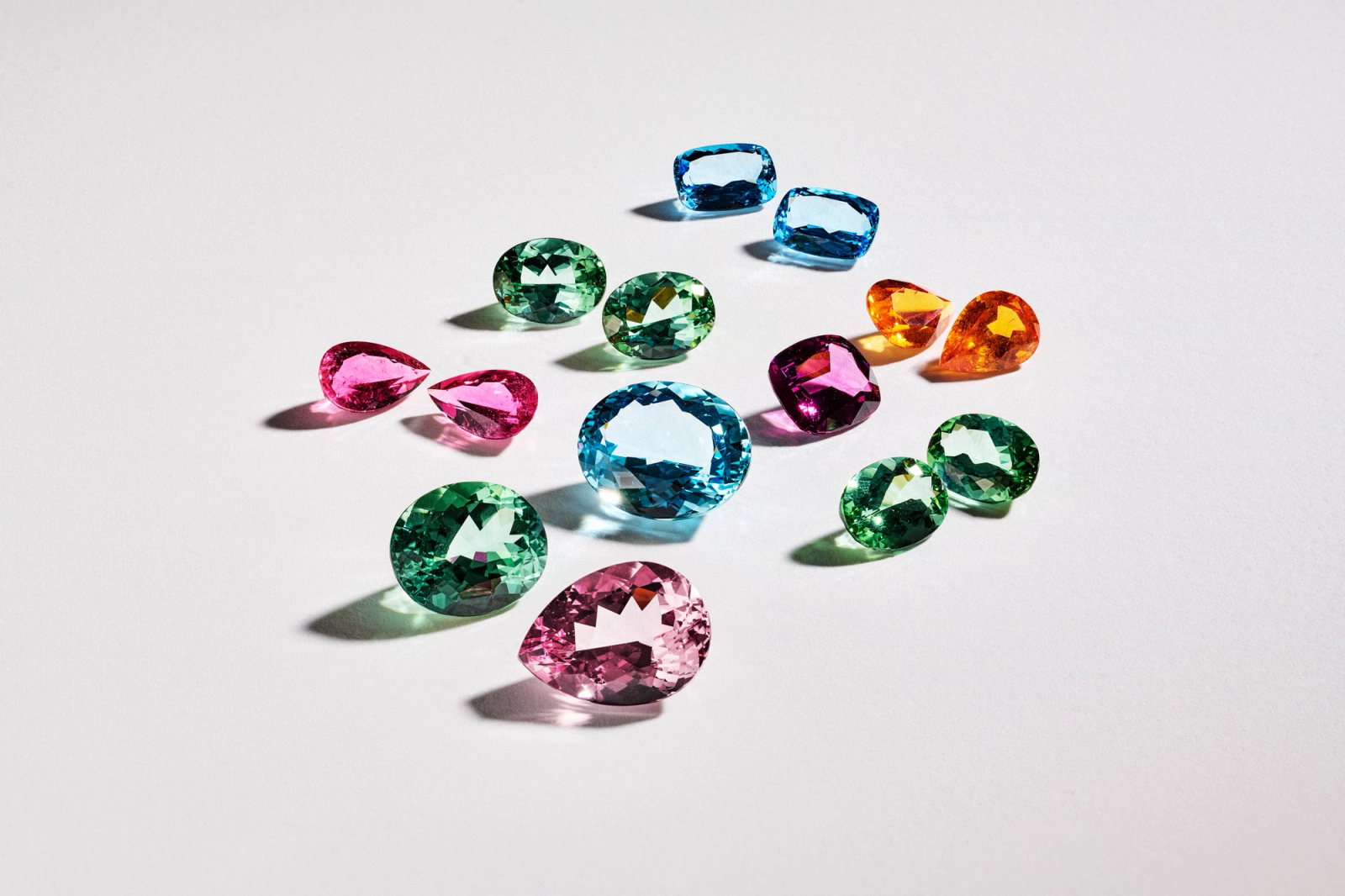 Assortment of colorful faceted gemstones in various shapes on a white background.