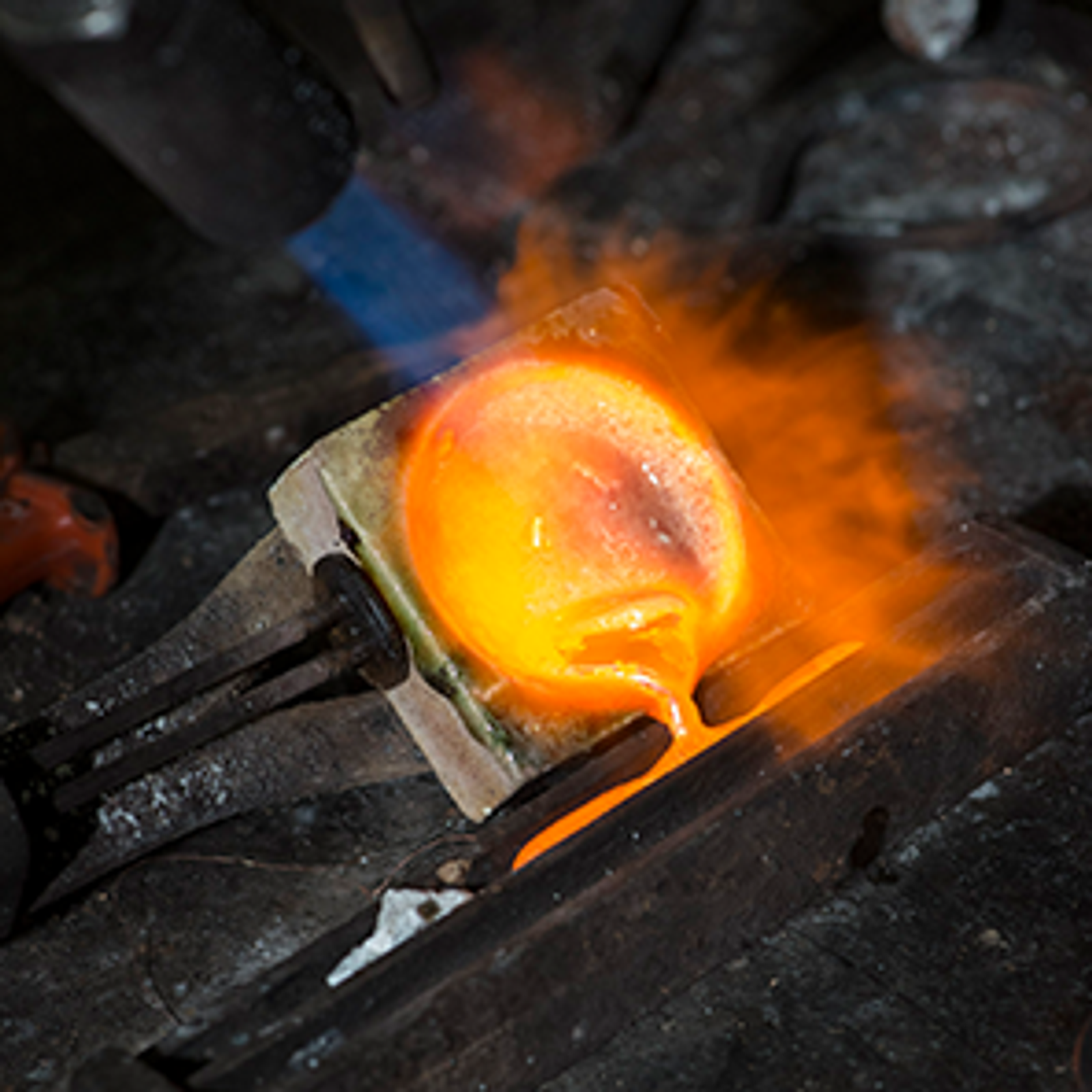 A torch heats glowing molten metal in a crucible.