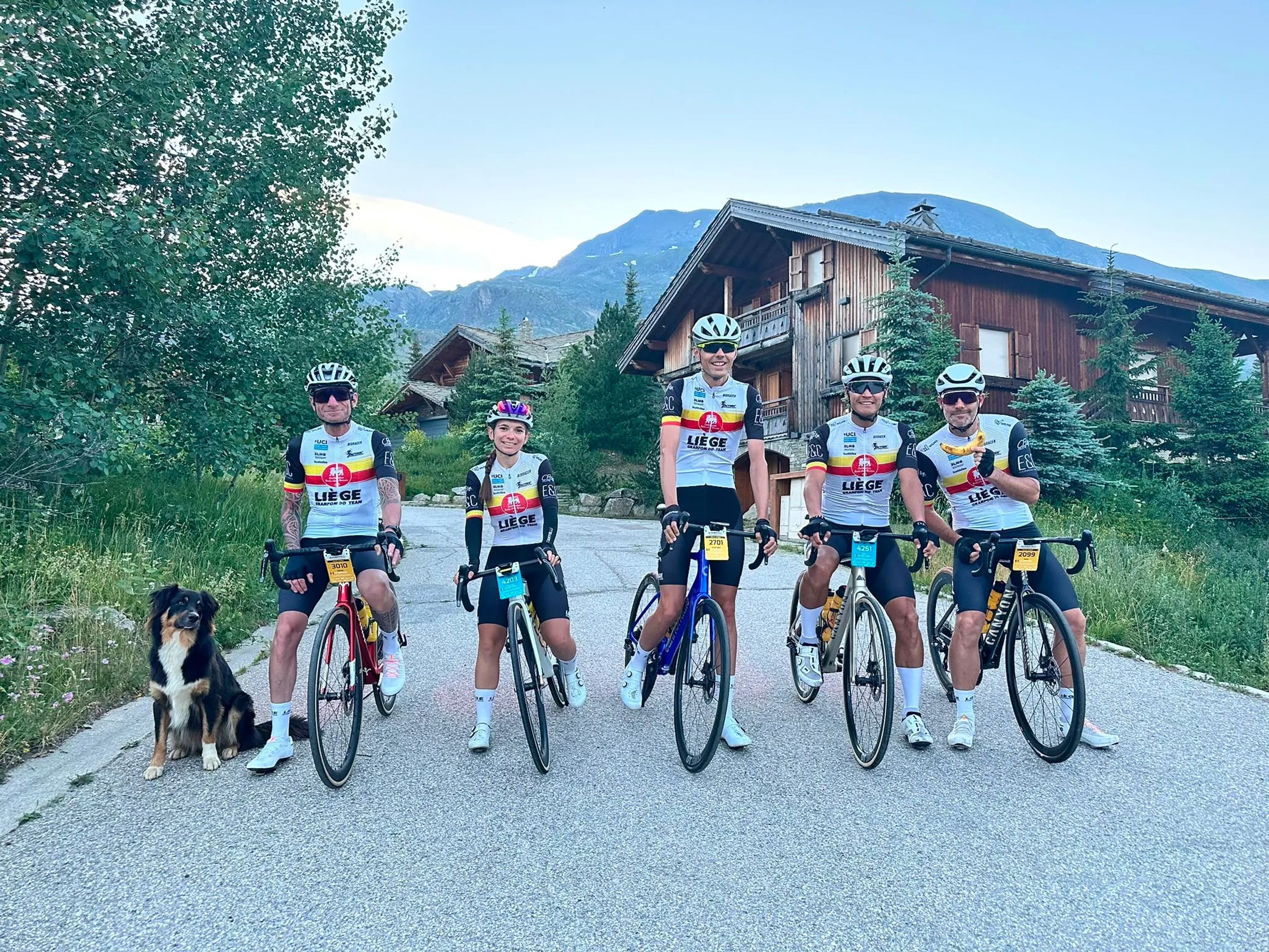 Cinq membres du team posent avec leur vélo et un chien devant un chalet de montagne