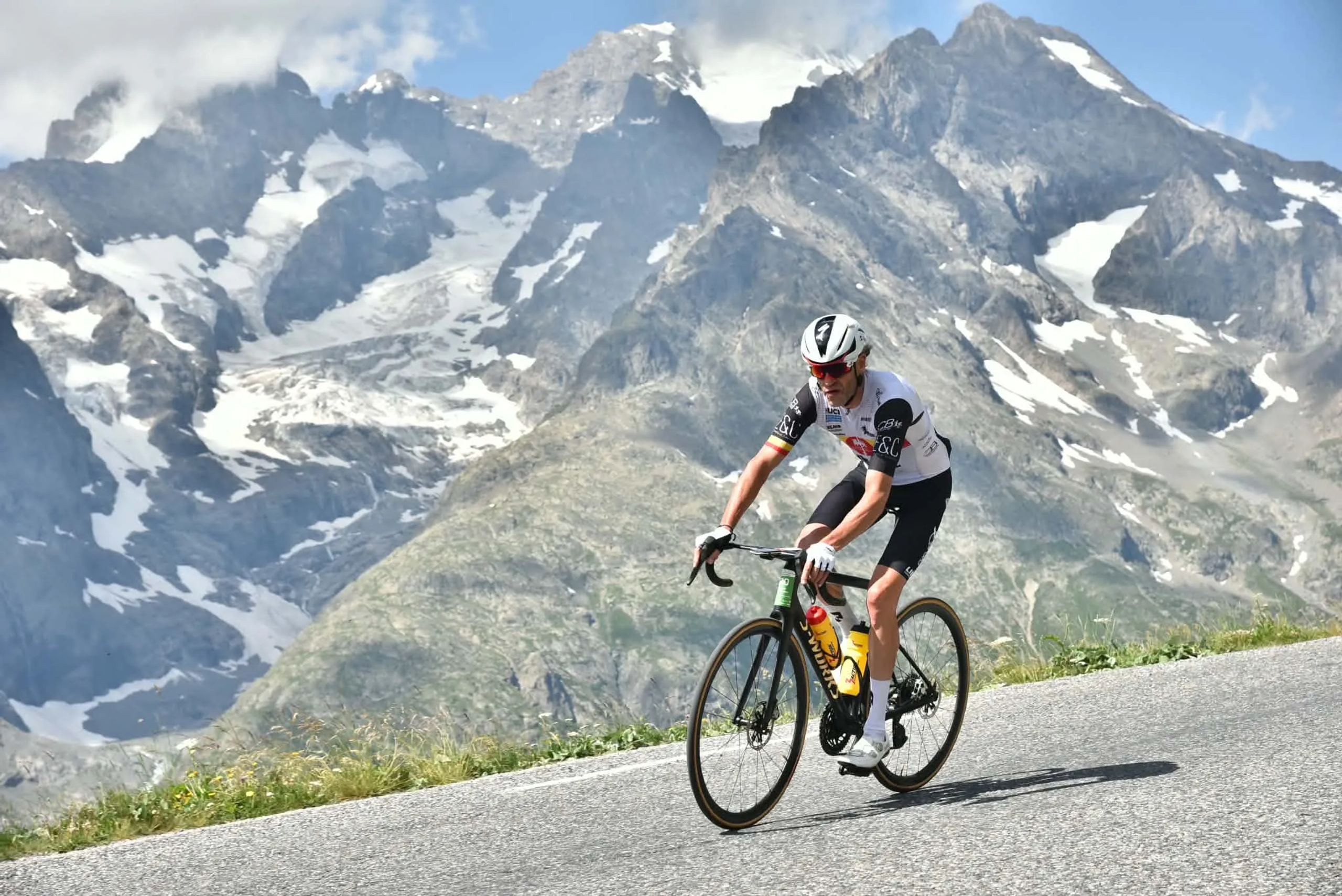 Coureur en maillot LGFT grimpant un col devant des sommets enneigés