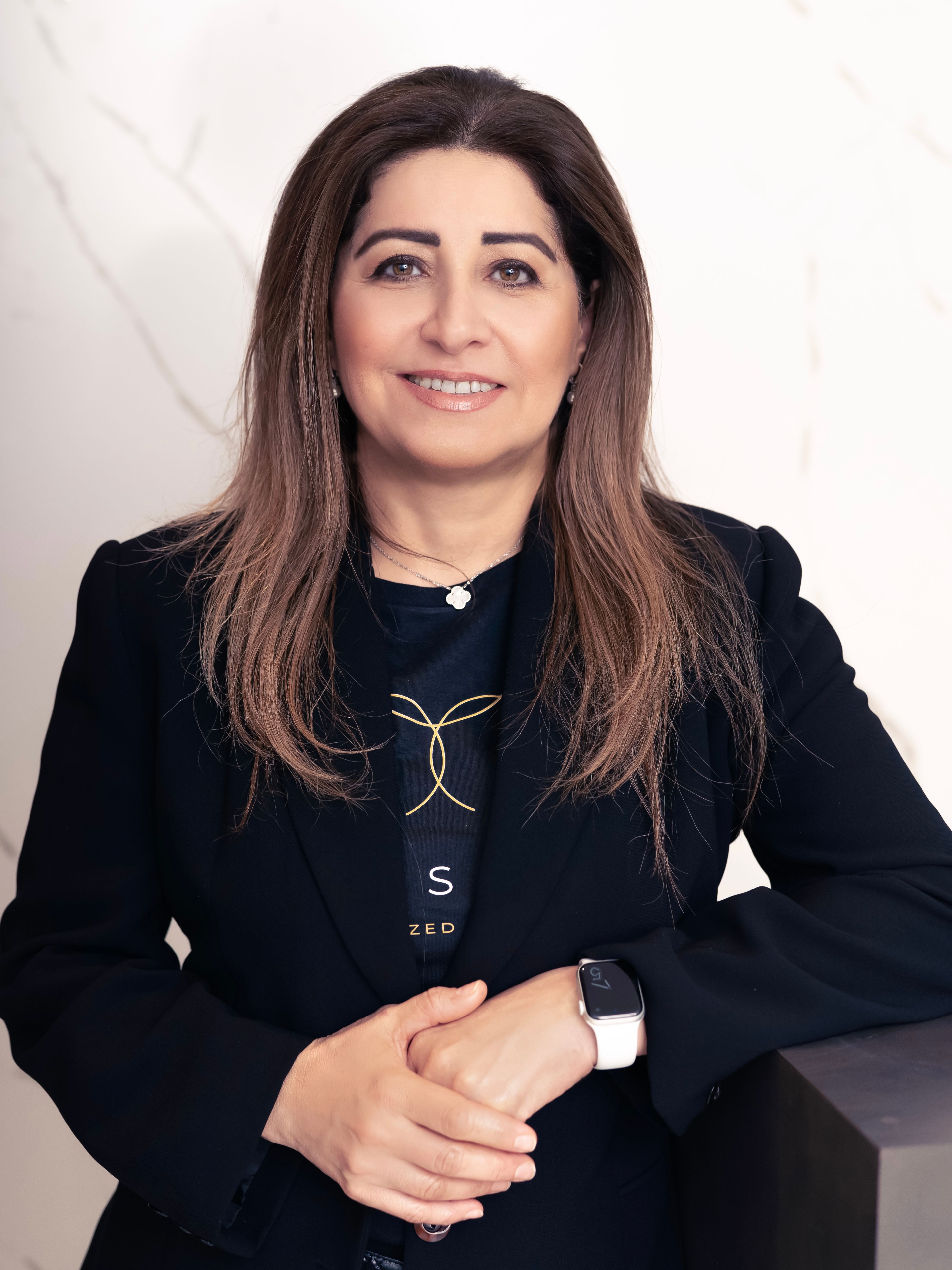 Portrait of Dr. Dalia Taher smiling in front of a white marble slab background.
