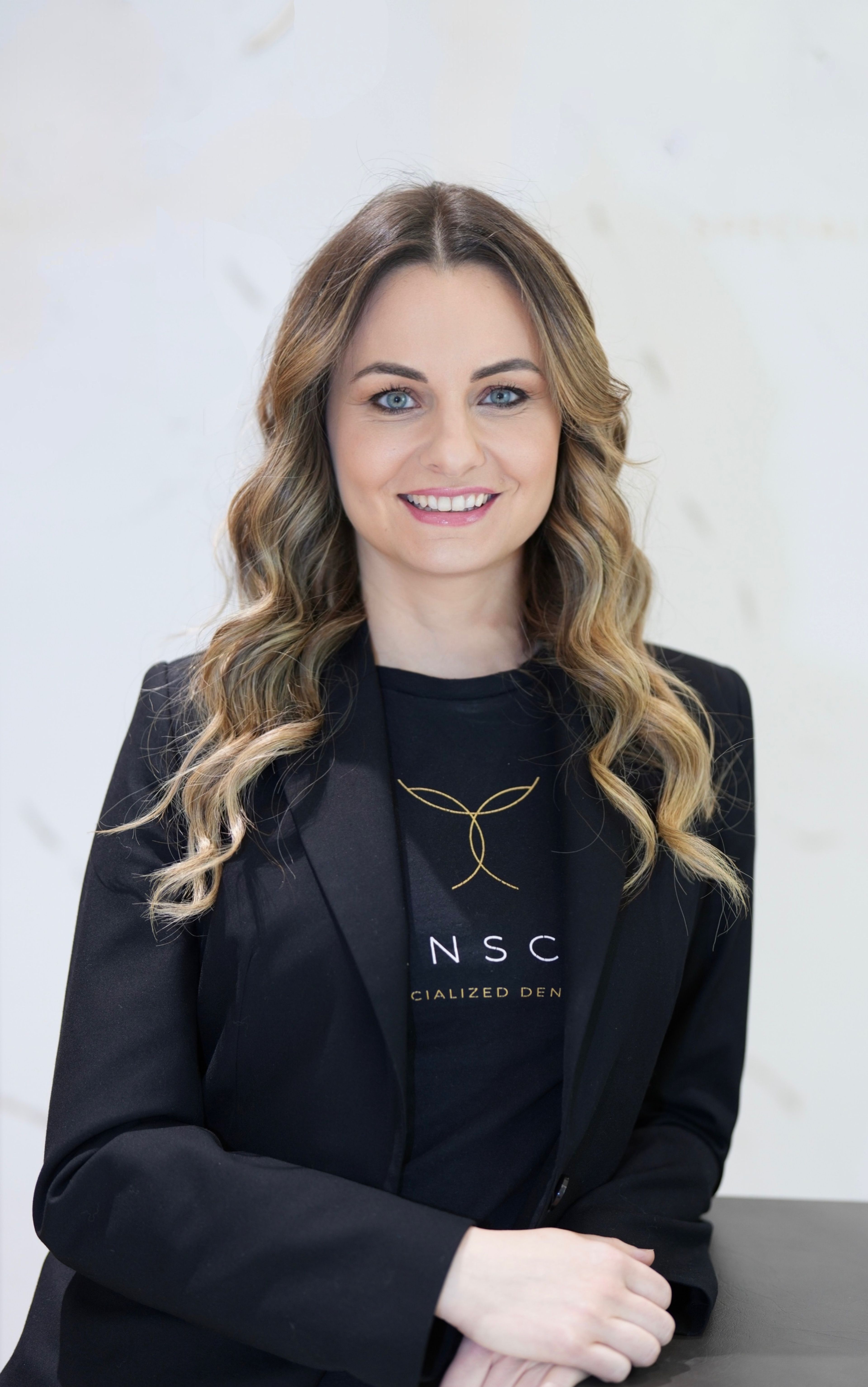 Portrait of Dr. Marijana Eic smiling in front of a white marble slab background.