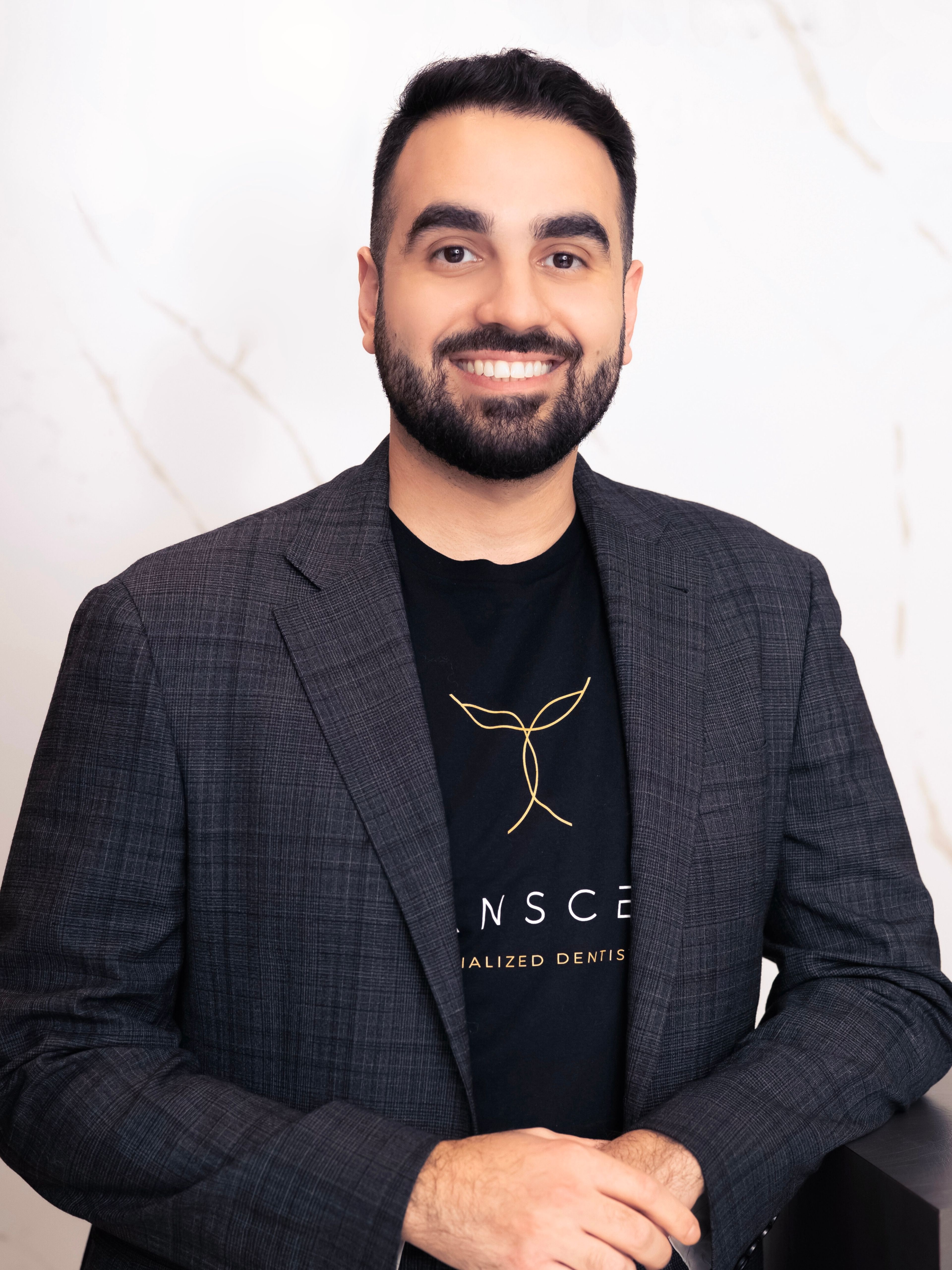 Portrait of Dr. Faraj Edher smiling in front of a white marble slab background.