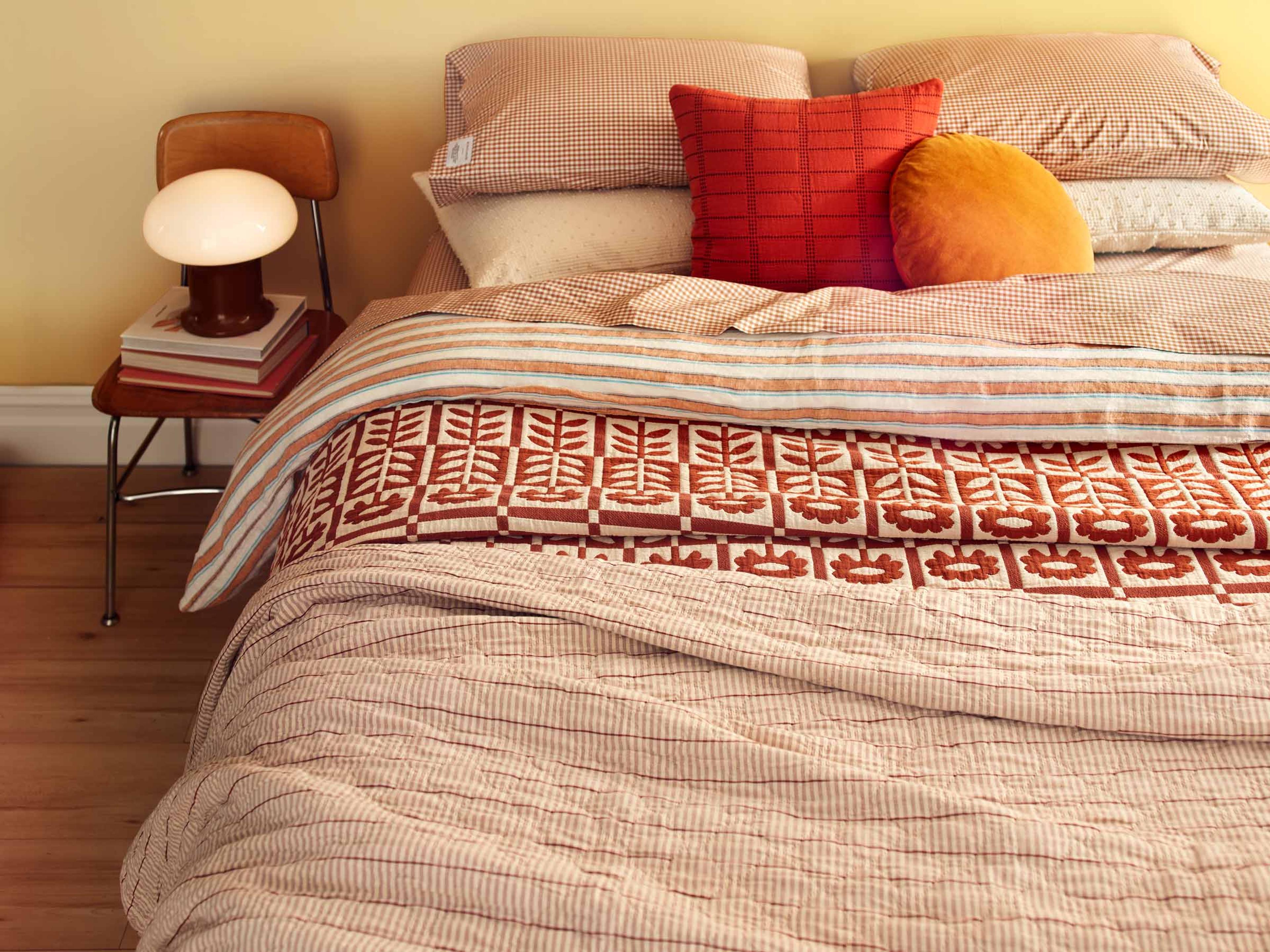 A bedroom with a floral quilt and a table lamp. 