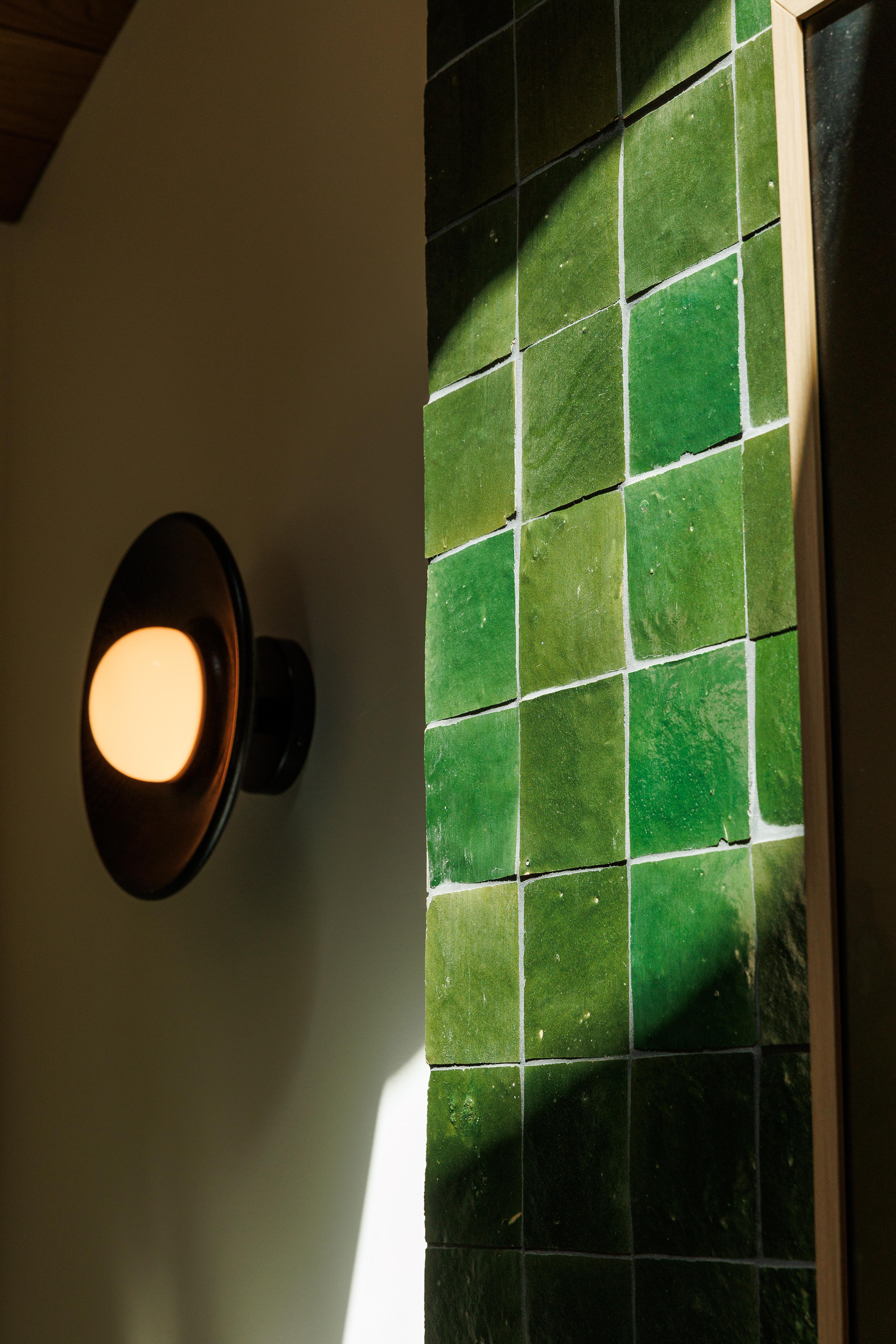 Close up of sconce in sunlight next to green tiles 