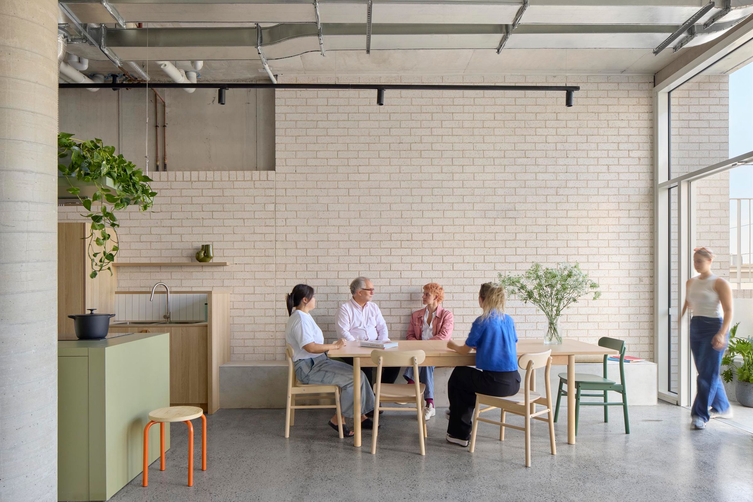 Photo of communal dining area next to communal kitchen. Four people are seated and talking at a large table.