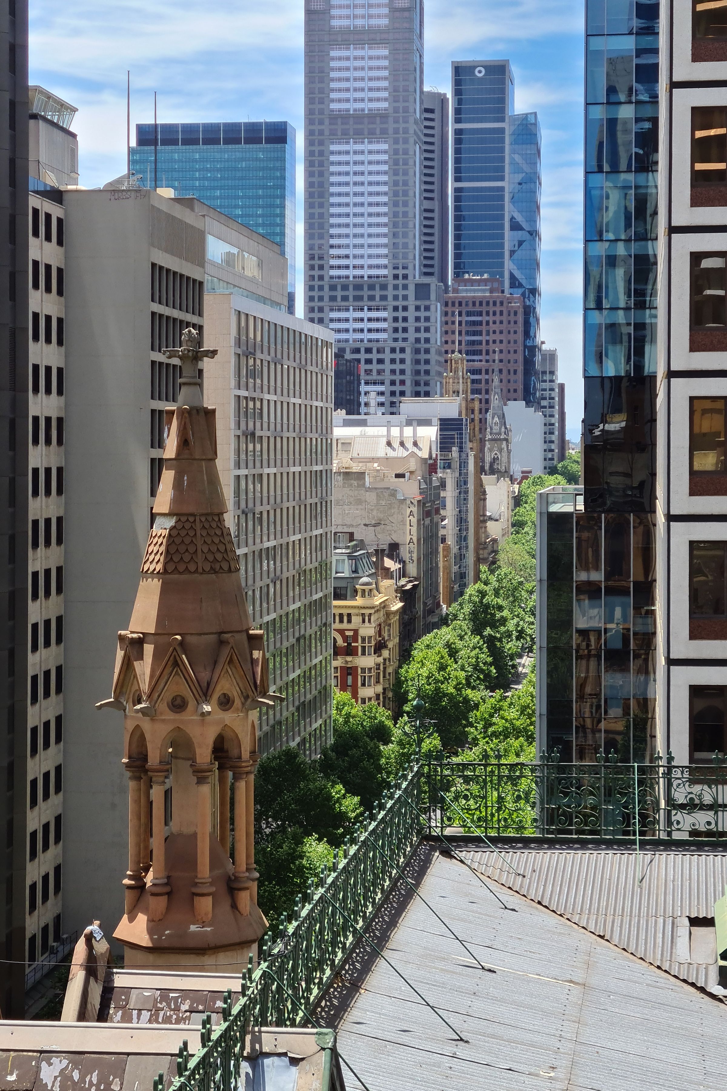 A view of a cityscape from a high perspective with a church spire in the foreground with modern high-rise buildings in the distance, heritage-style buildings at the street level and a tree-lined street
