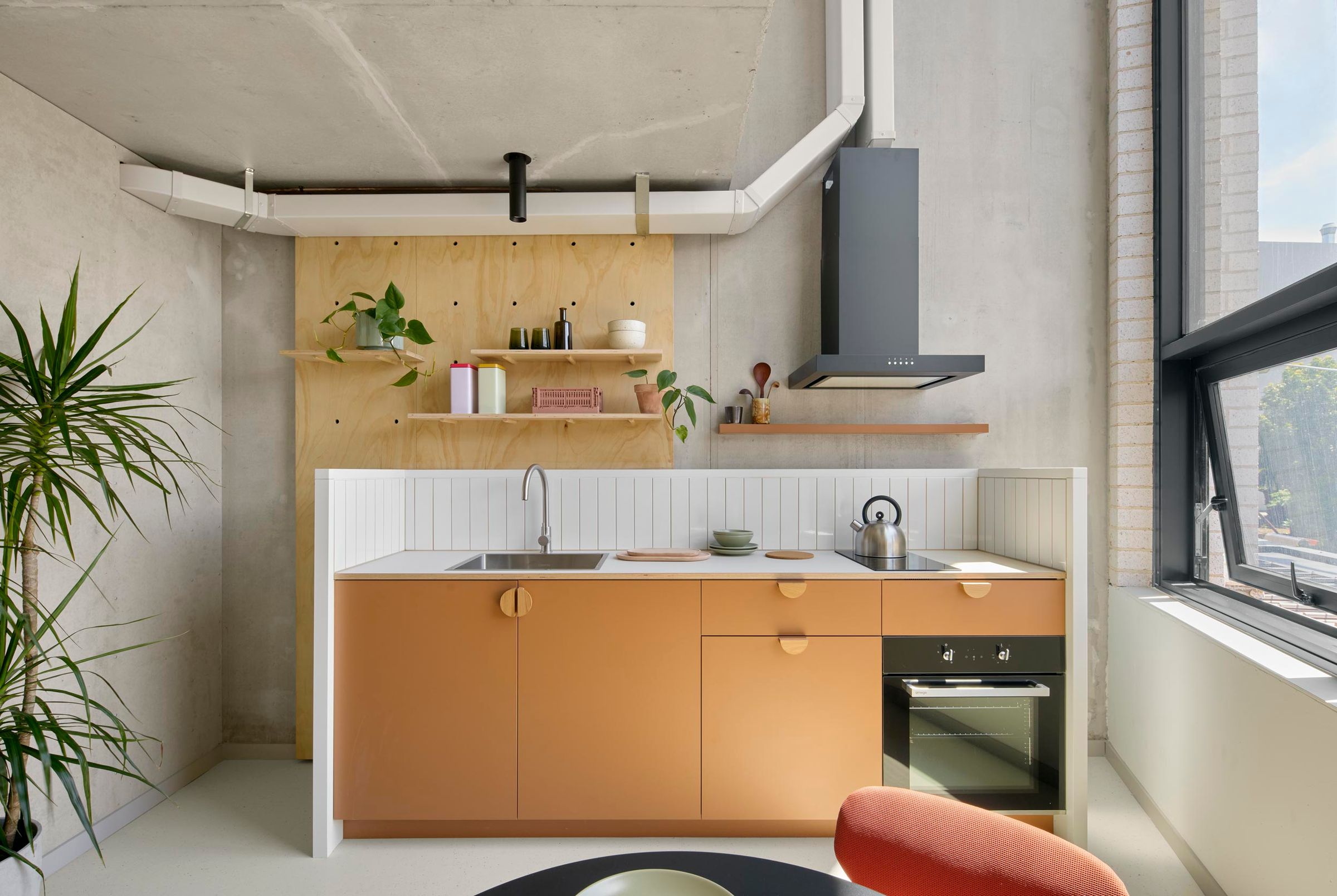 Photo of Teilhaus kitchen showing galley kitchen with orange paint and timber materials.