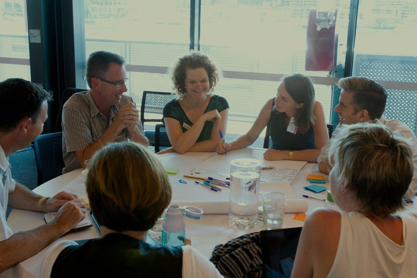 A photograph of participants of the 2017 City Resilience Exchange. The photograph shows a group of people sitting around a table writing down their thoughts and ideas.