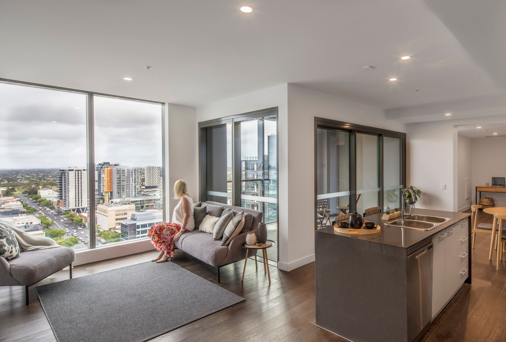 Photo of retirement living apartment, showing an open plan living, kitchen, dining area. There is a large living window in the living room with a long-distance view over the city.