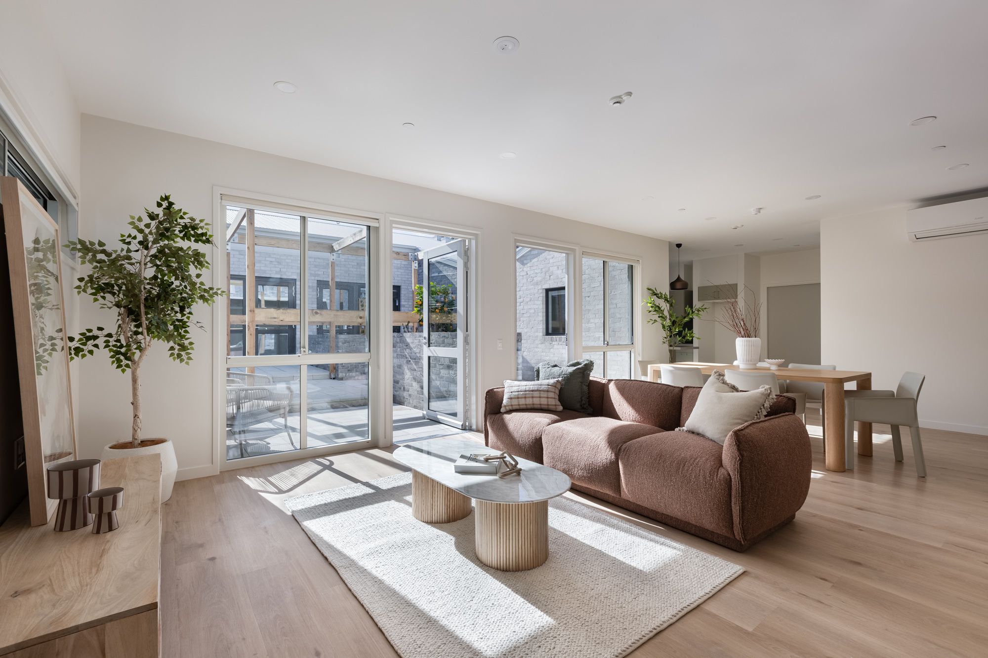 View of open plan living and dining room looking out to a sunny courtyard.