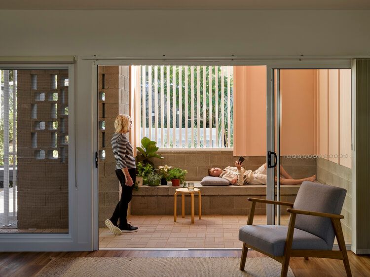 Photo of living area connected to private outdoor space through large sliding doors. A woman and child are in the private outdoor space chatting.