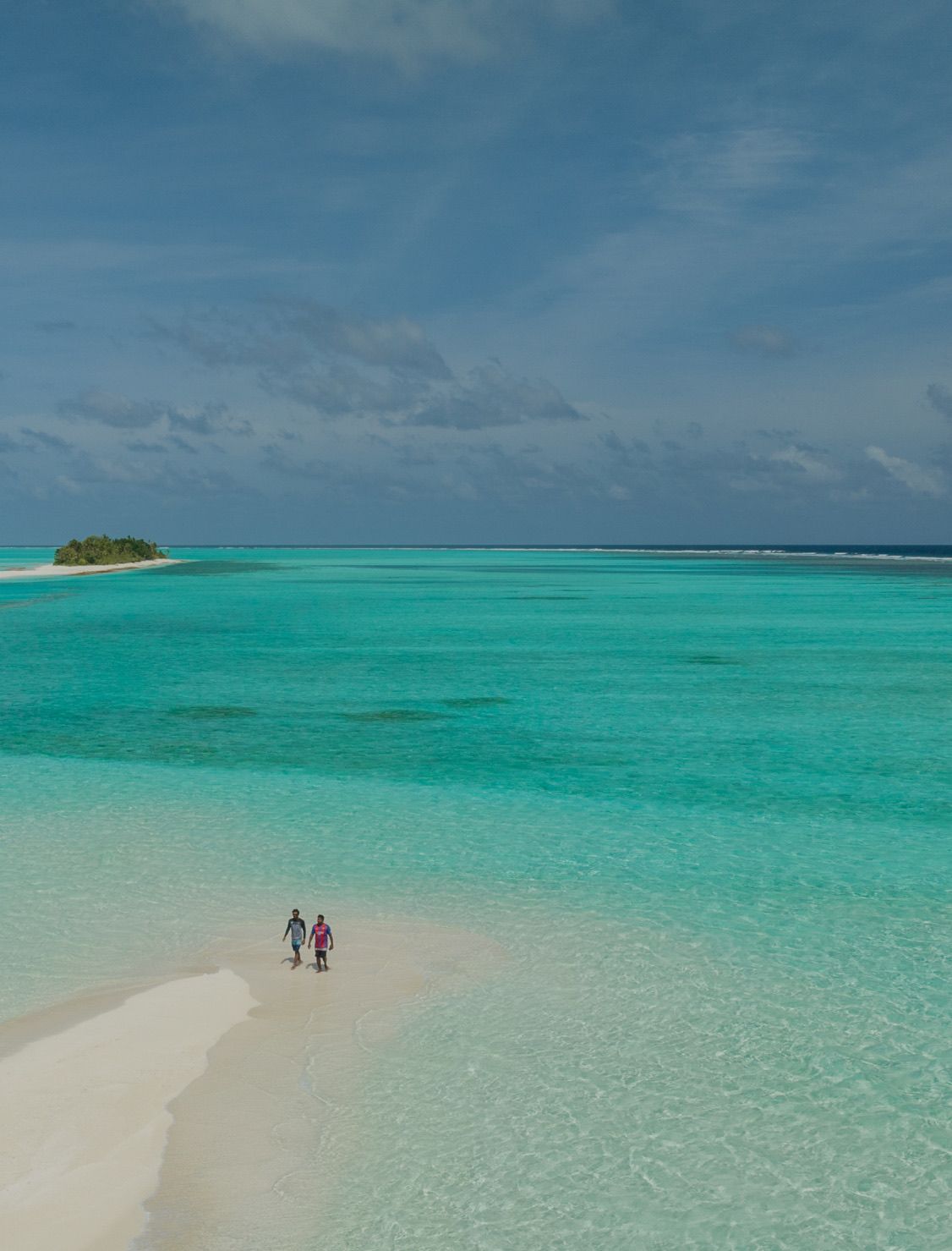 A sandbank curving into the lagoon, two figures walking