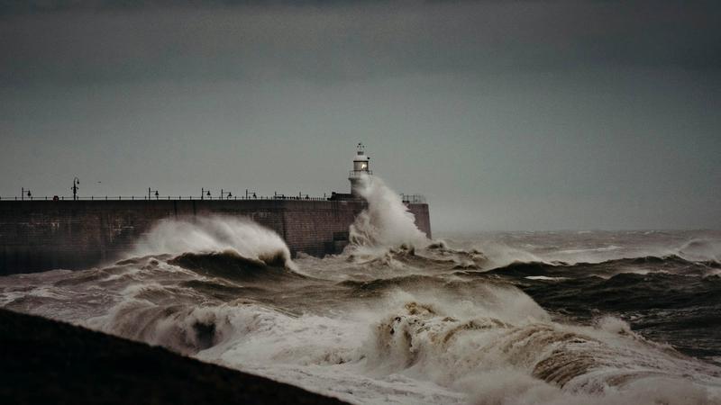 Heavy waves crashing against a sea wall during a storm, illustrating extreme weather risks the UK faces.