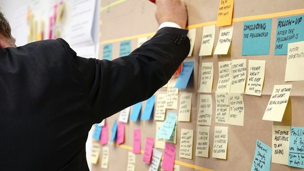 A person pinning a handwritten note onto a board already covered in written notes grouped under headings