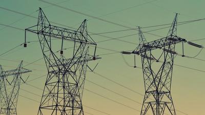 Electricity transmission pylons and power lines silhouetted against an orange sunset sky.