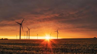 Wind turbines in a green UK landscape under a bright sky, representing the electrification at the heart of the Seventh Carbon Budget