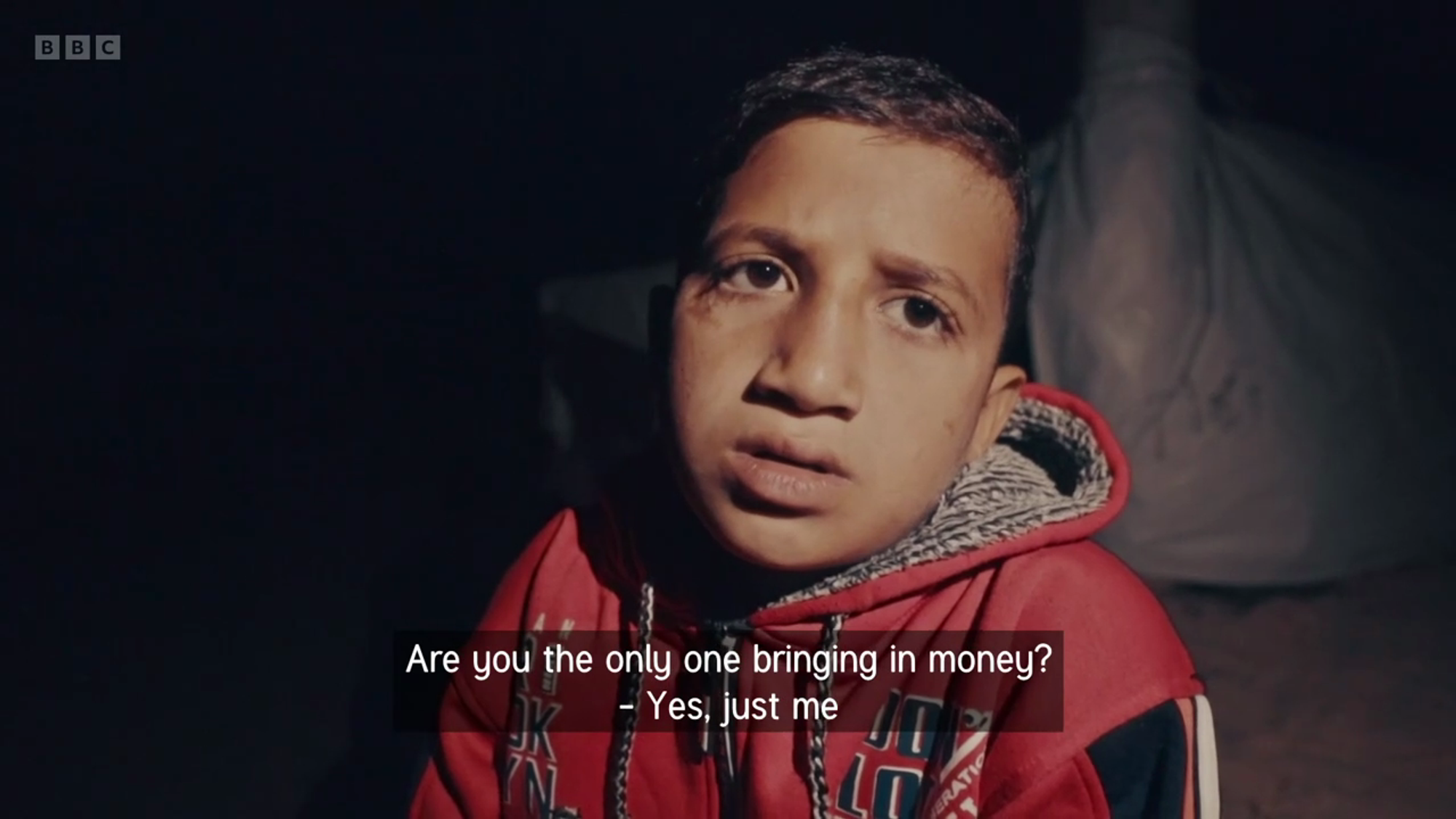 a video still of a young Palestinian boy being interviewed. a closed caption reads: 'Are you the only one bringing in money? - Yes, just me'