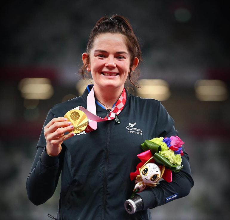 a woman in a black jacket holds up a gold medal