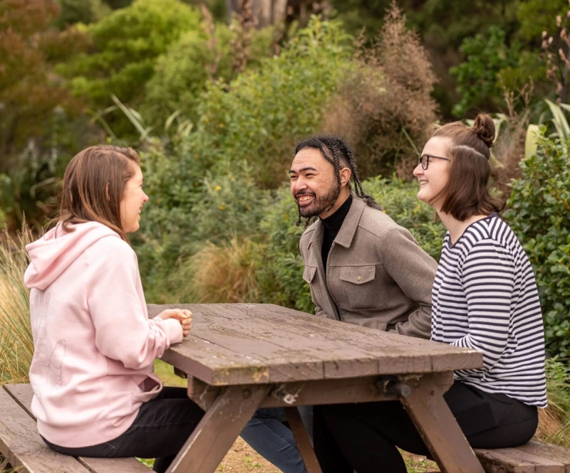 a man and two women sit at a picnic table a man and two women sit at a picnic table