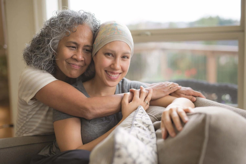 a woman with cancer hugging another woman on a couch