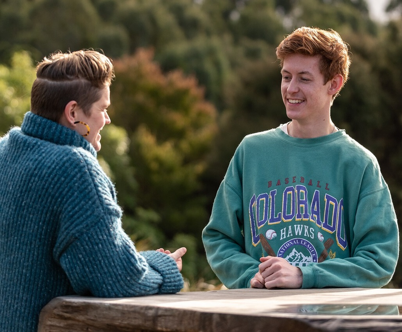 a man wearing a green colorado hawks sweatshirt talks to a woman